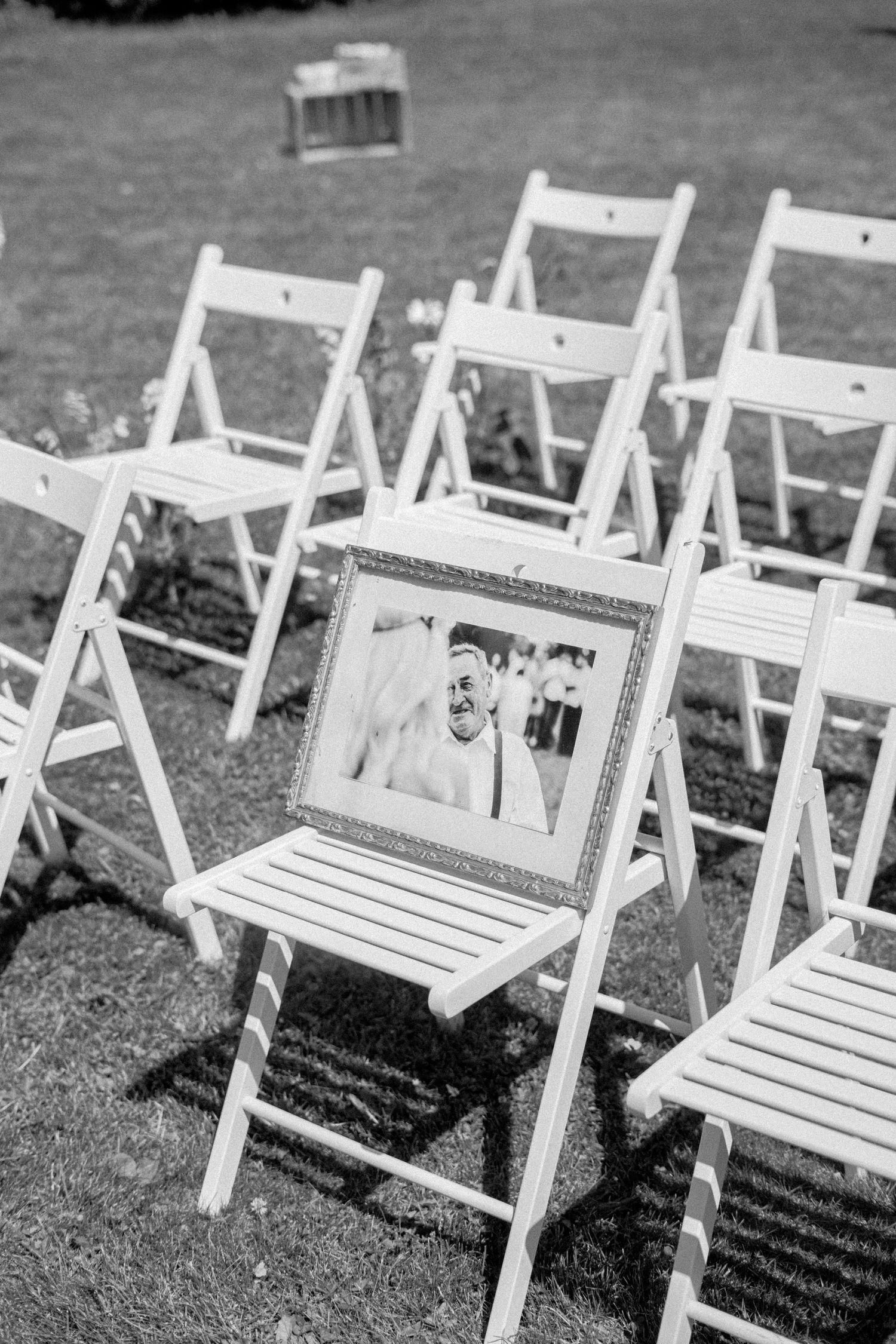 A row of empty white wooden folding chairs arranged on grass for an outdoor ceremony or event.