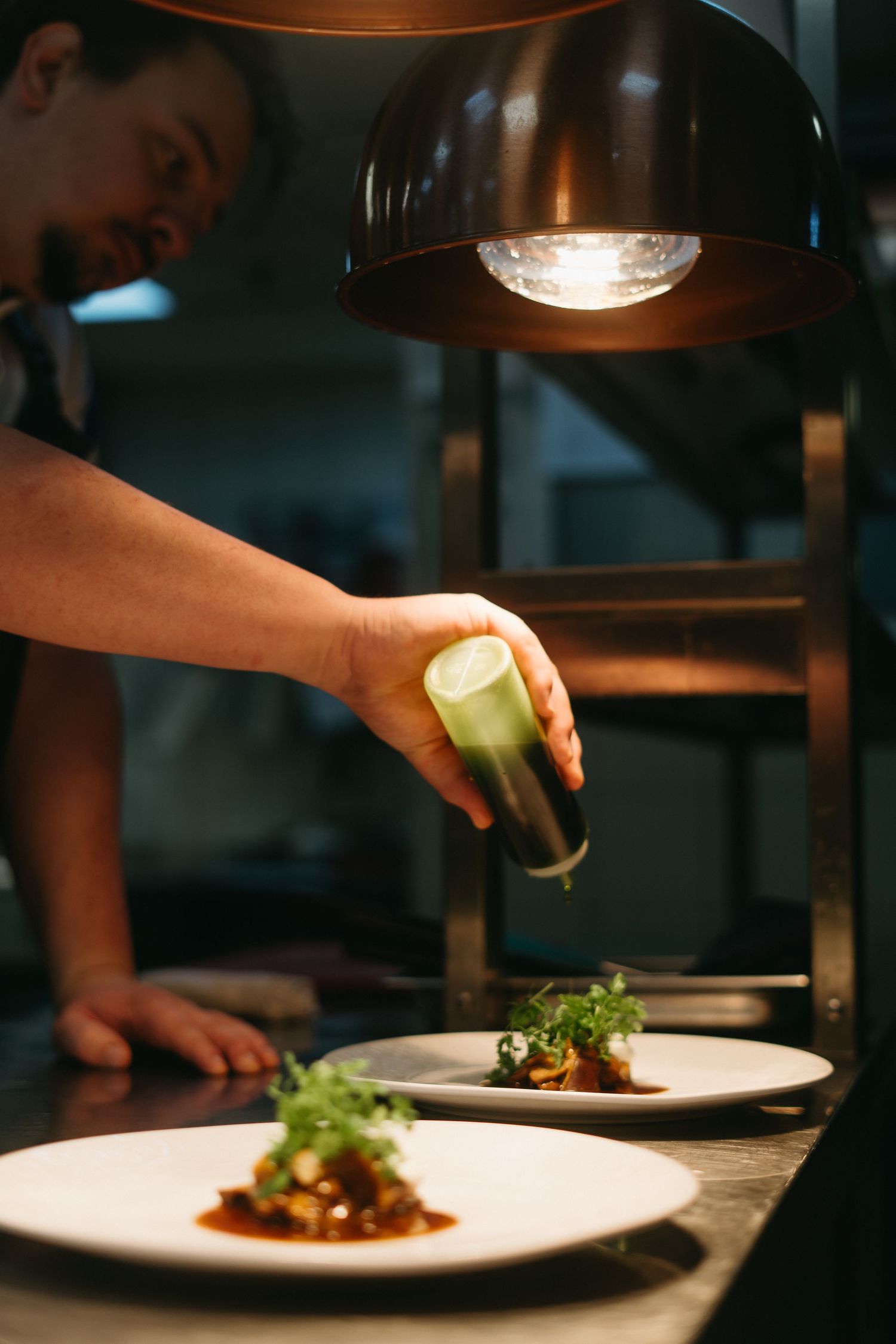 Chef garnishing elegant plated dishes under warm restaurant lighting.