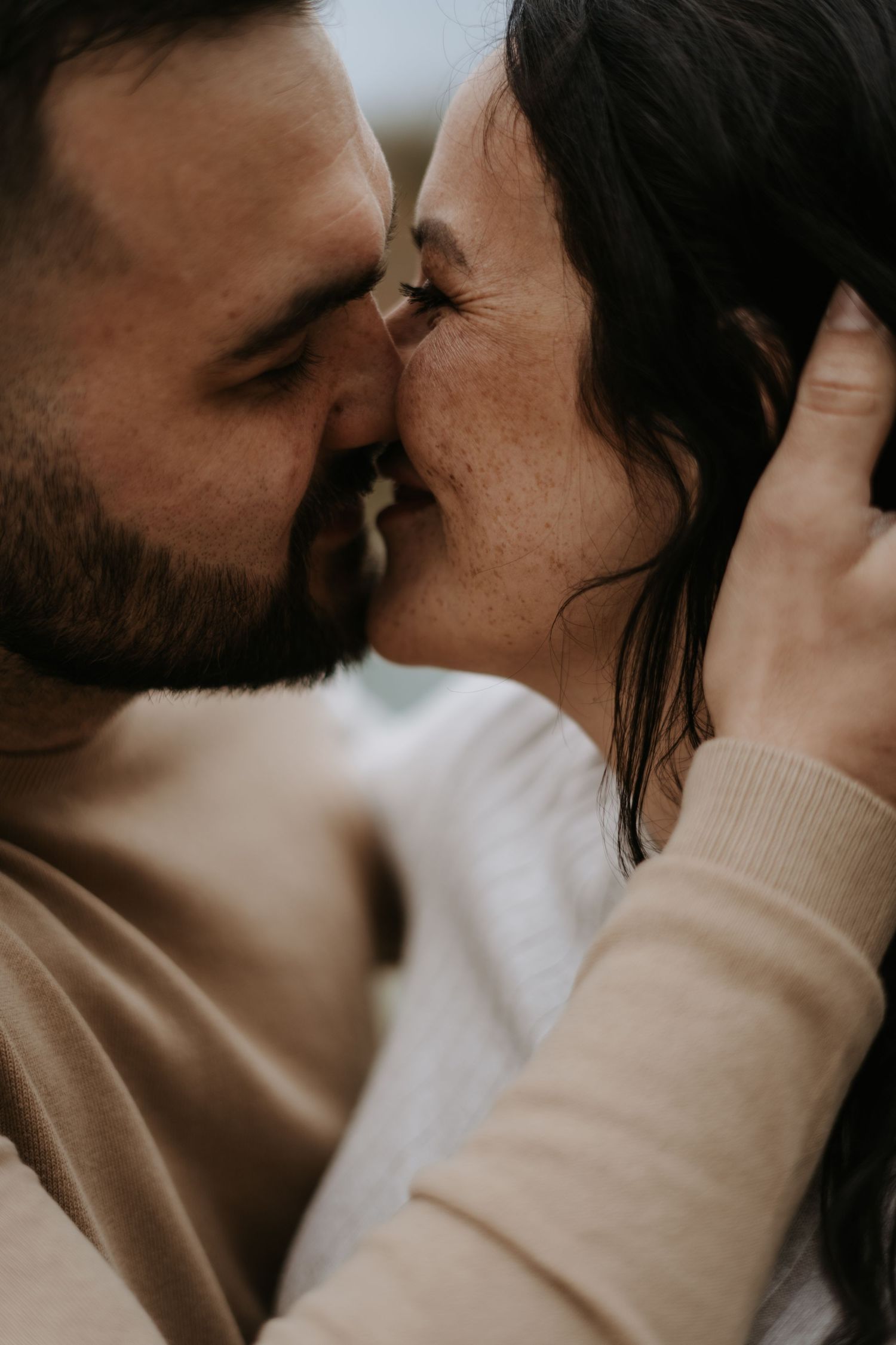 Close-up intimate moments captured between couple in neutral tones during maternity session.