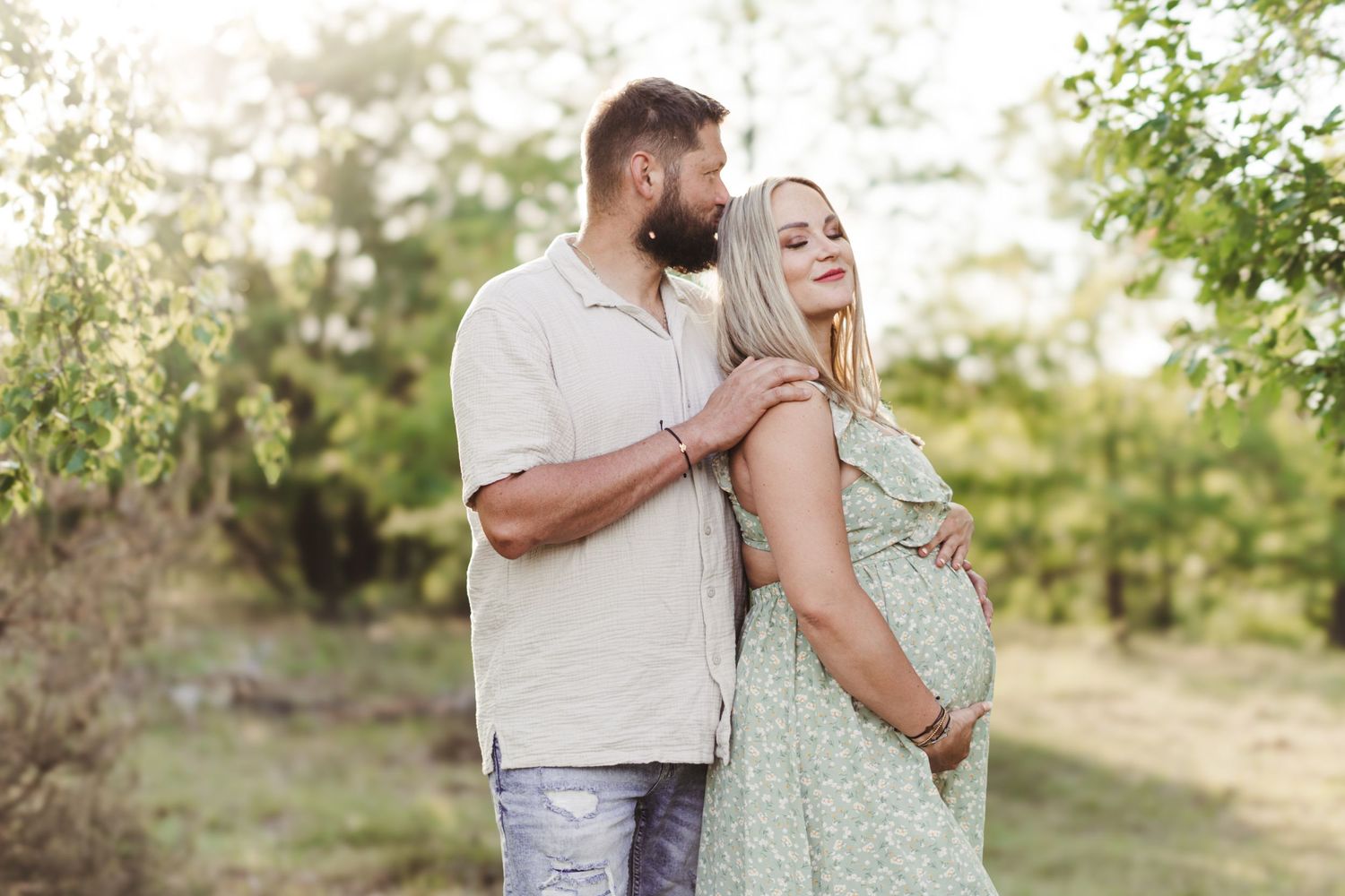 Maternity photoshoot in nature with couple embracing during golden hour.