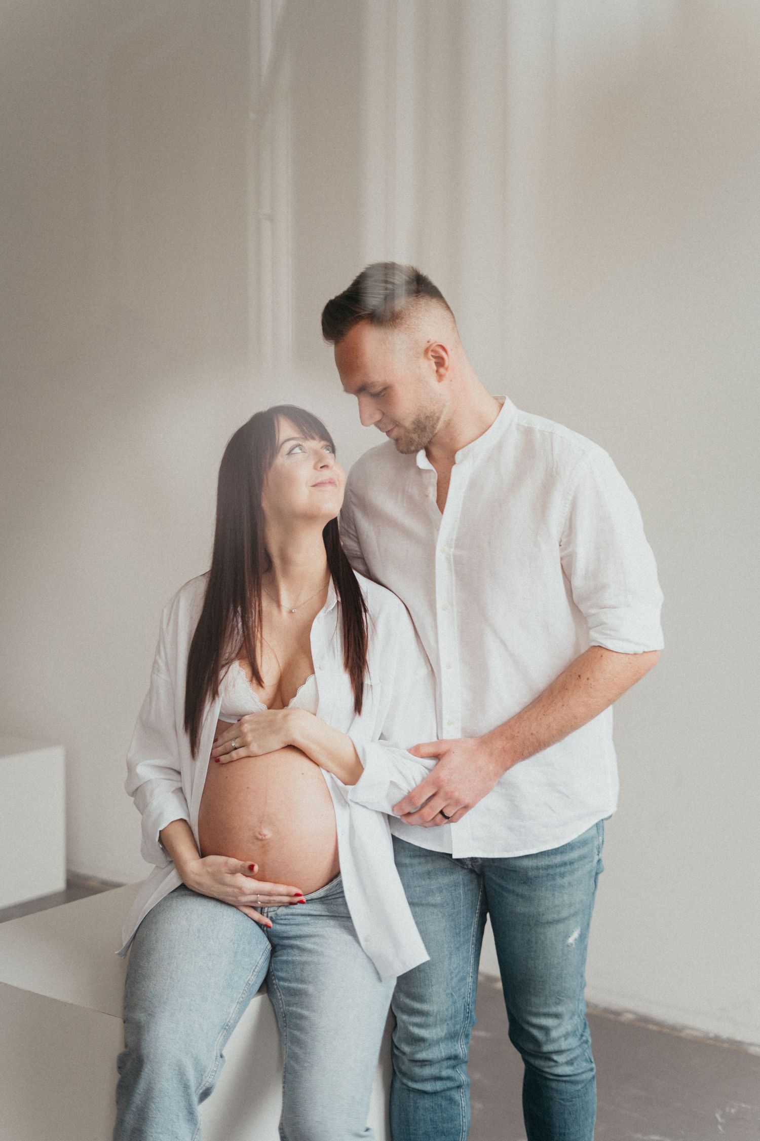 A couple shares an intimate moment during their maternity photoshoot in a bright minimal setting.