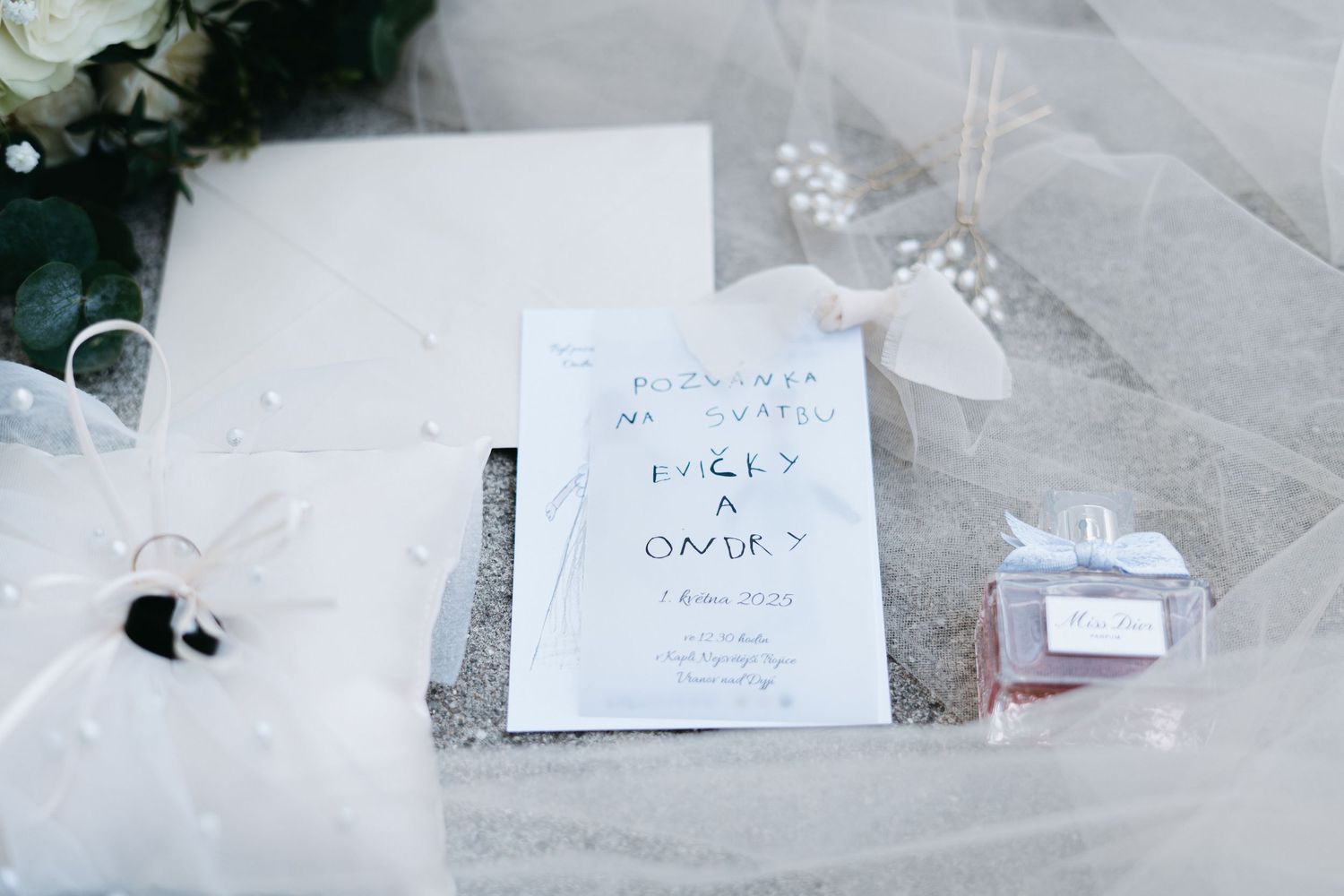 White wedding invitation card laying on tulle fabric with decorative elements nearby.