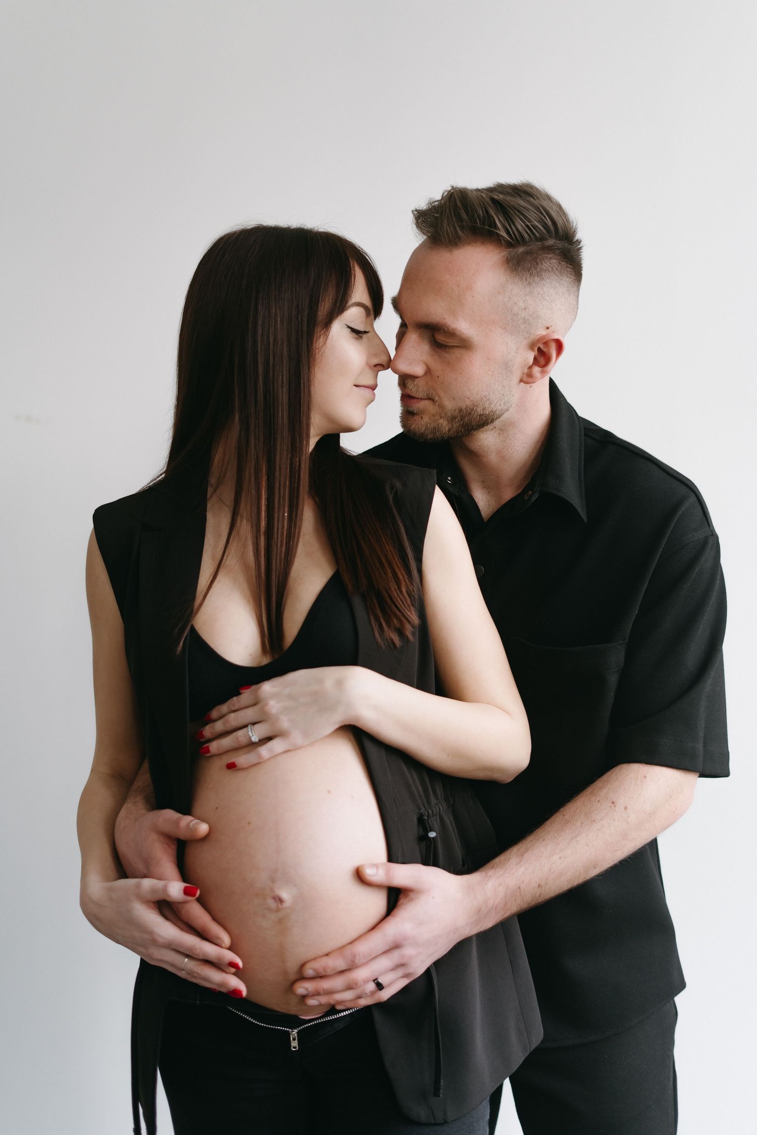 Intimate maternity portrait showing tender moment between couple in black outfits.