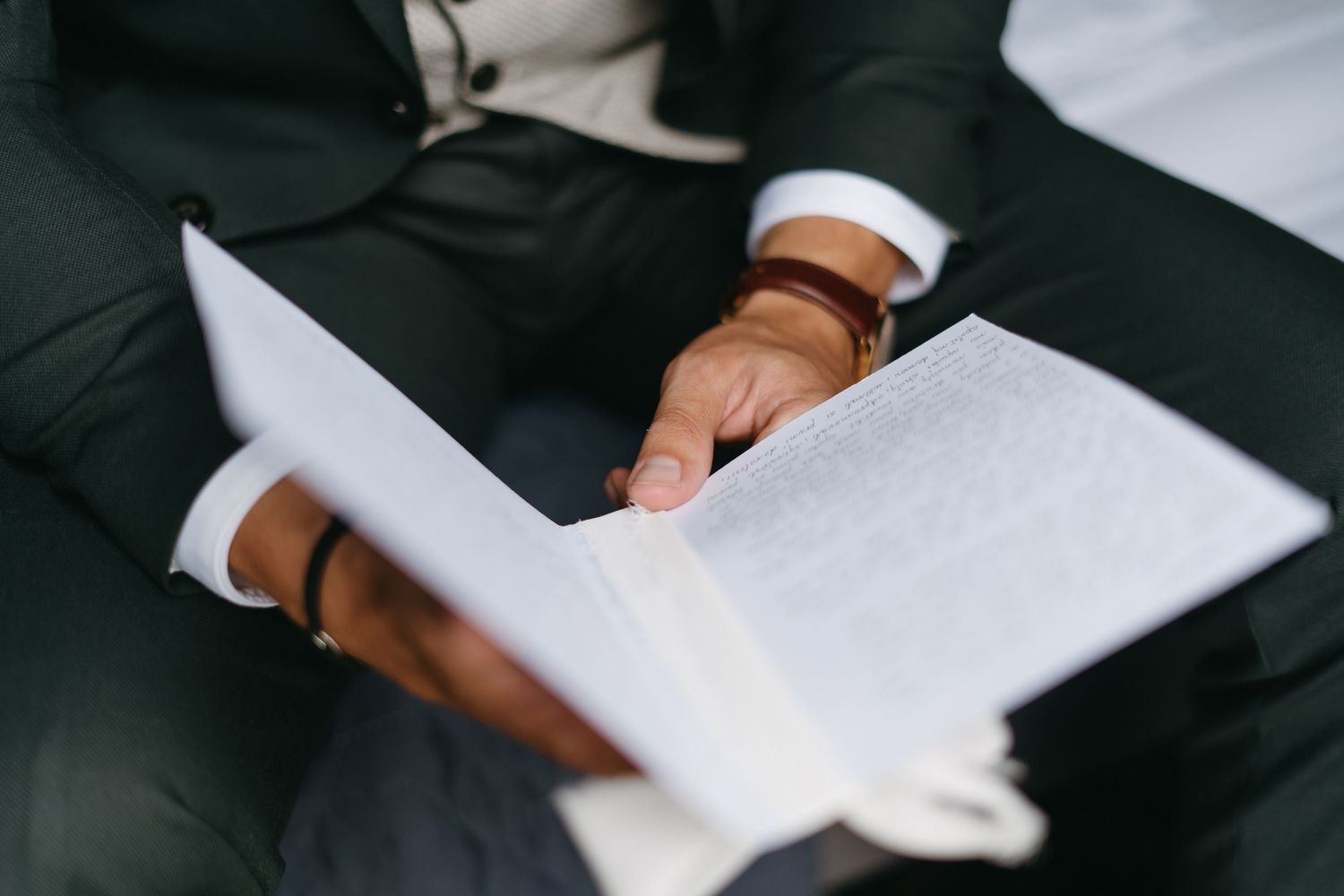 Close-up view of a person signing multiple business or legal documents with a pen on a dark surface.