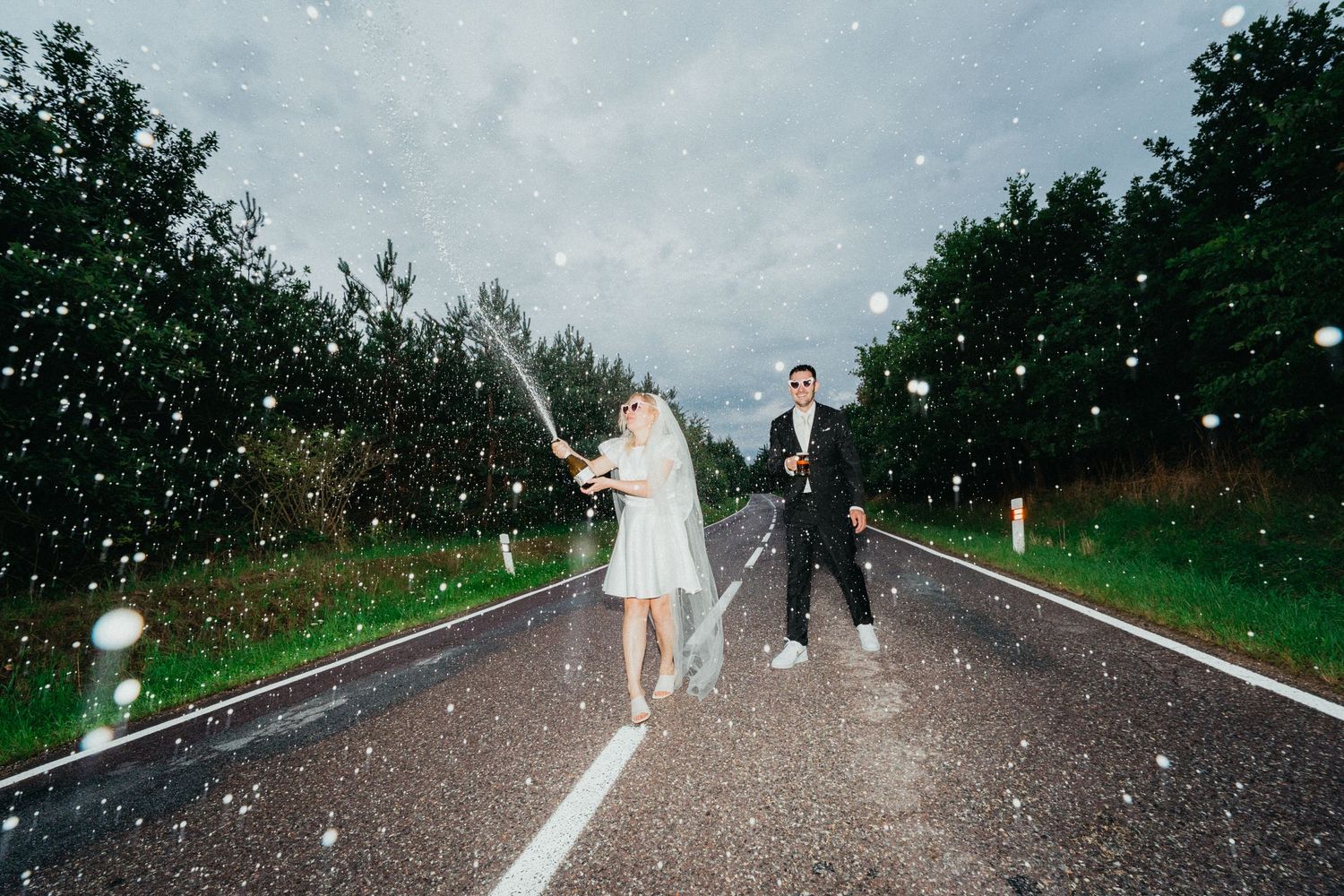 A couple walks up the road as flower petals fall around them during a wedding celebration.