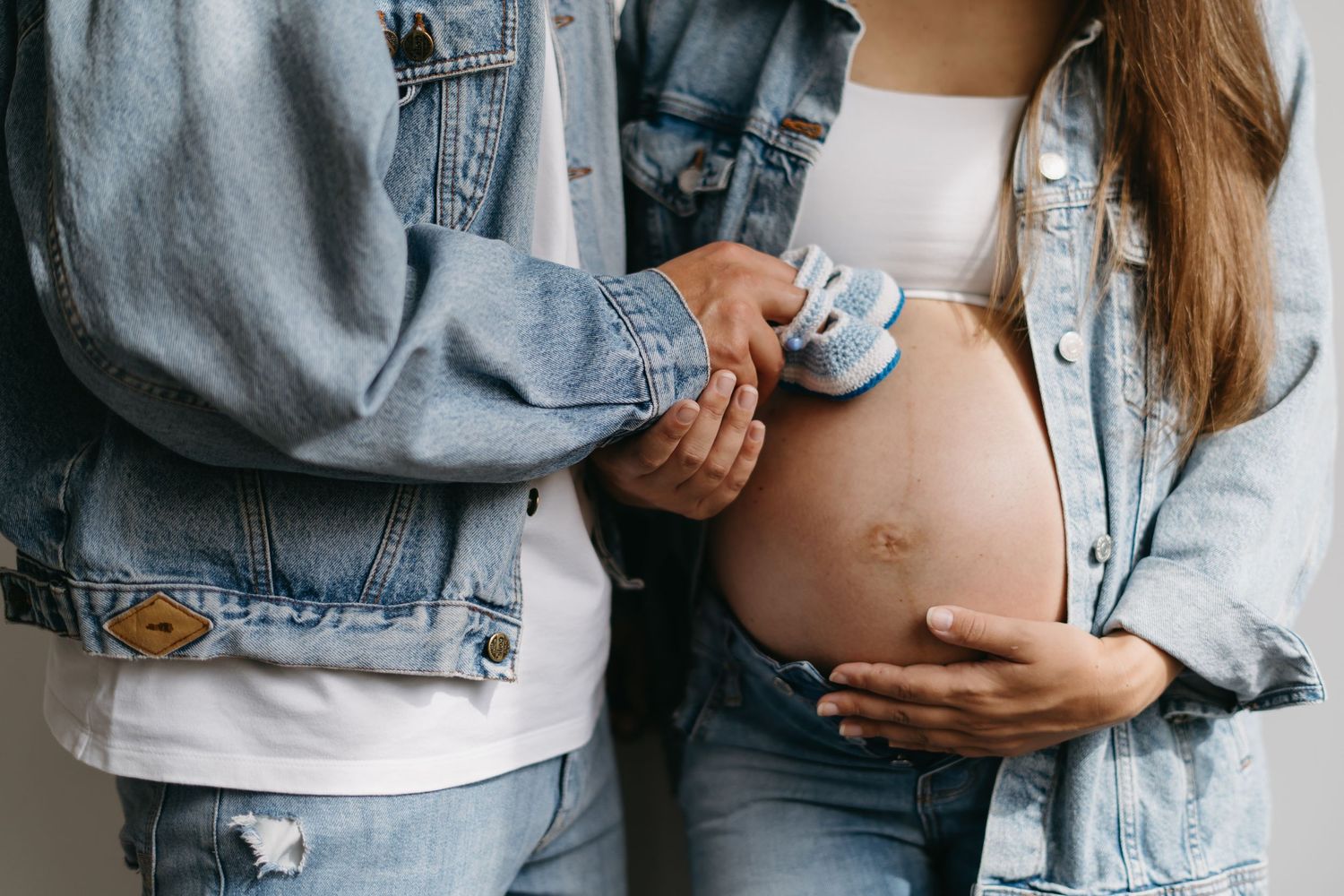 Close-up of couple holding tiny blue baby shoes against pregnant belly.