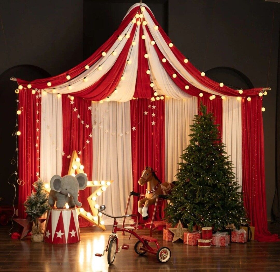 Festive circus-themed Christmas display with red drapes, string lights, toy elephant, rocking horse, tricycle, and decorated tree.