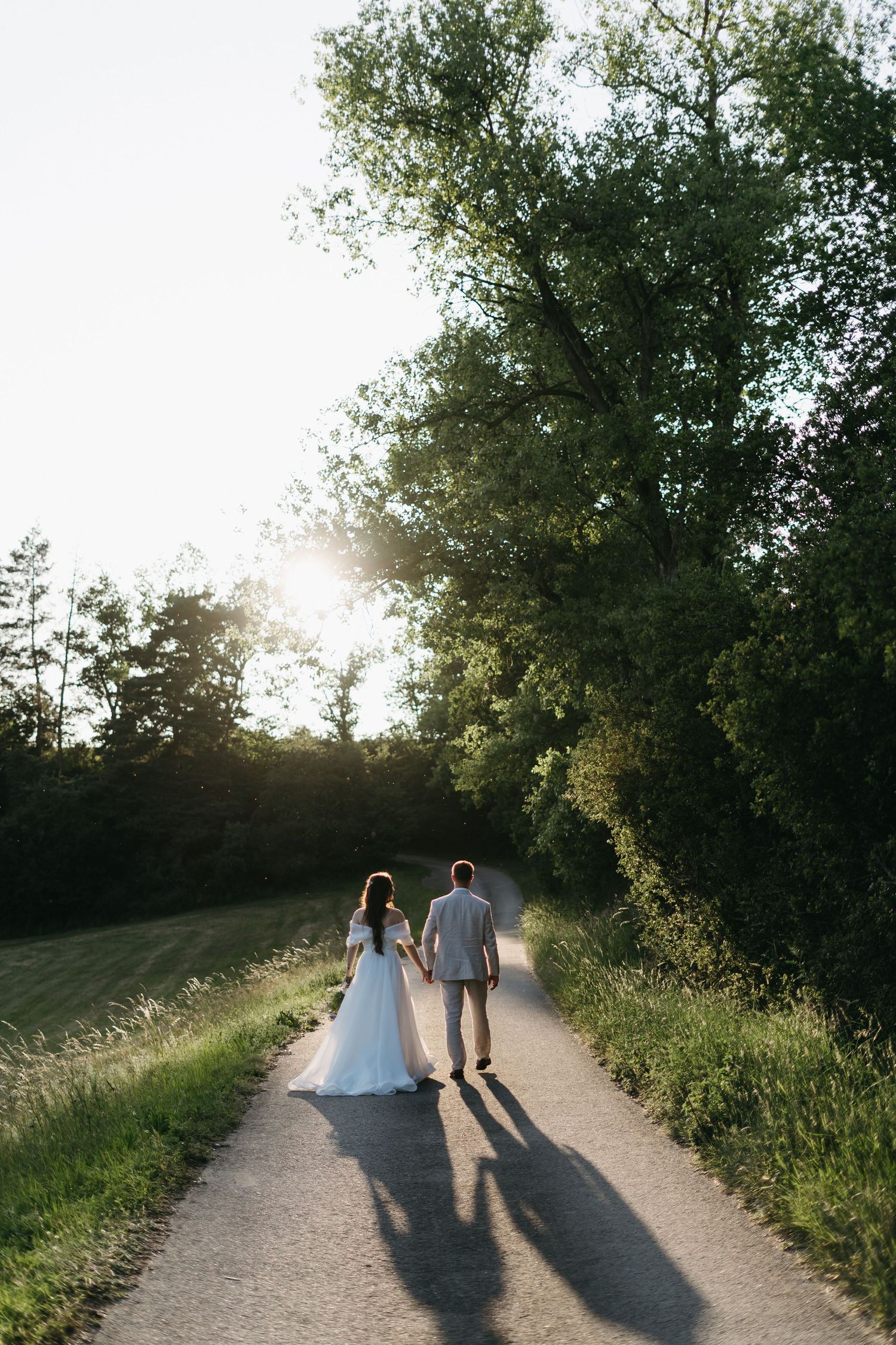 A couple walking along a sunlit rural path together casting long shadows during golden hour.