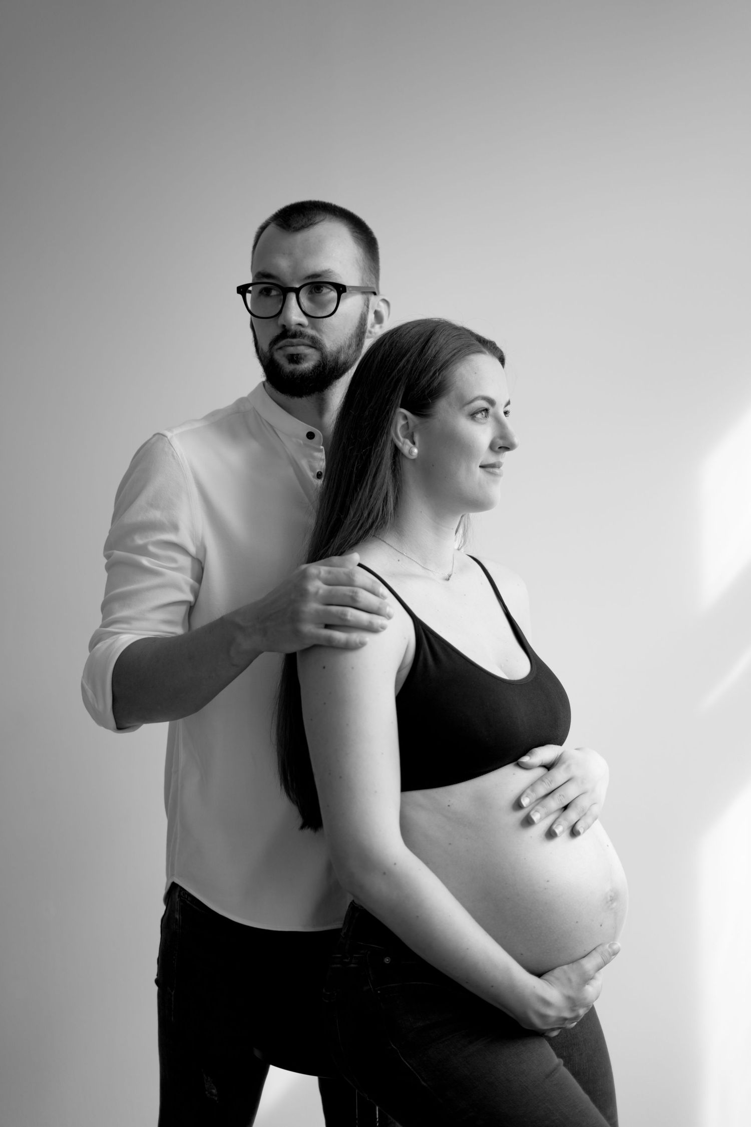 Intimate maternity photoshoot with couple in black and white against minimalist background.