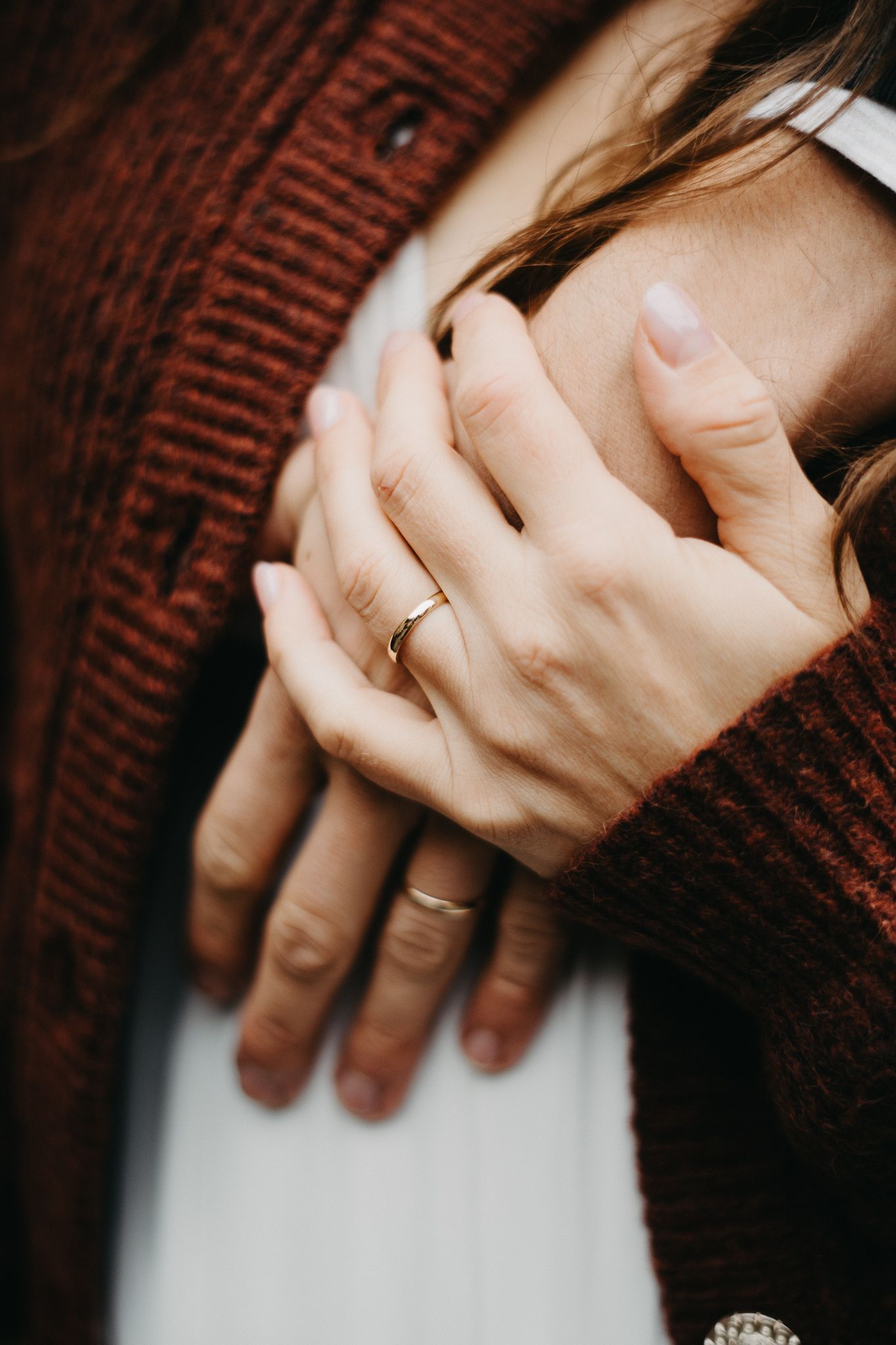 Close-up photo series showing hands wearing simple gold wedding rings against a brown knit sweater and white backdrop.