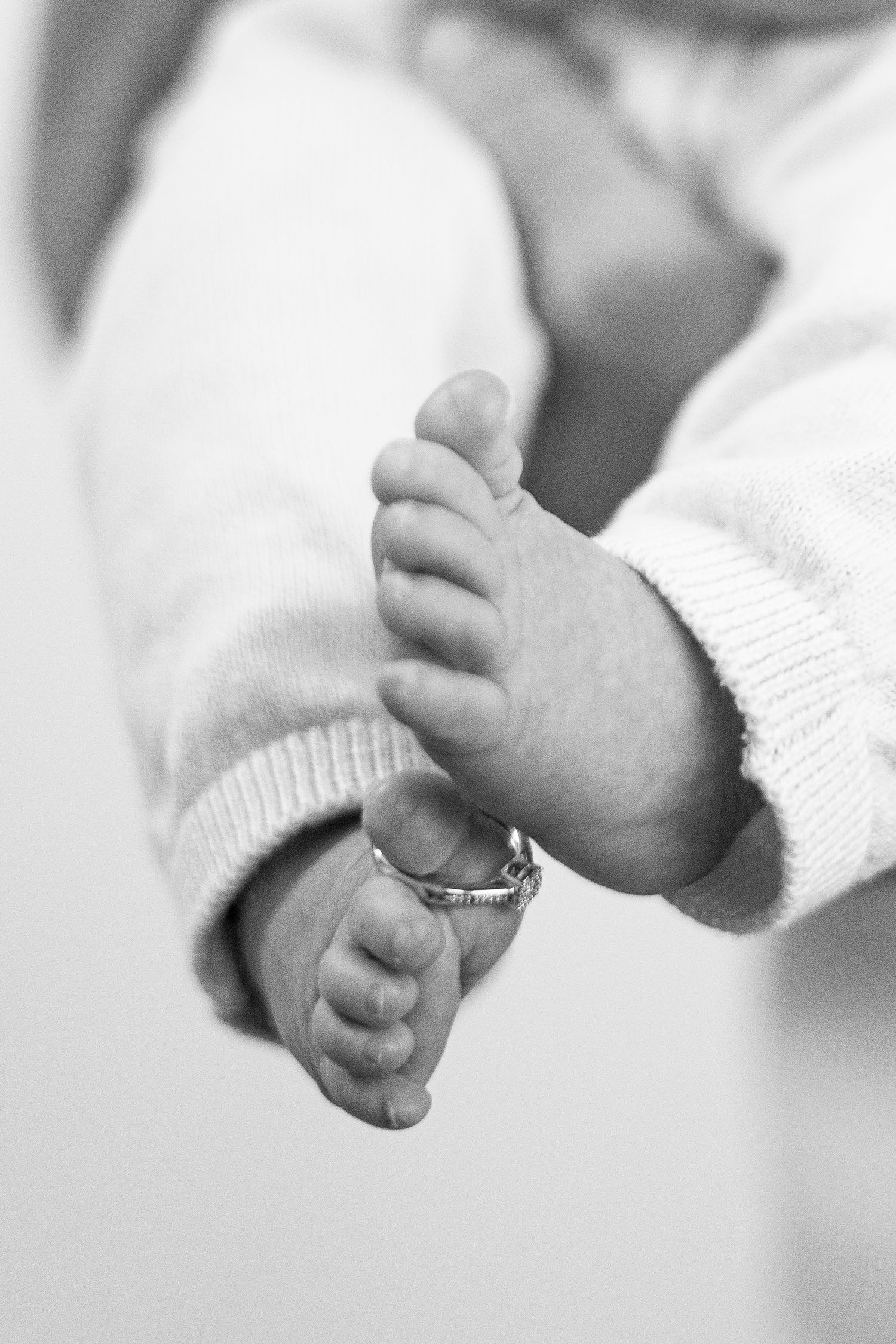 Baby's tiny feet with wedding rings captured in black and white intimate portrait.
