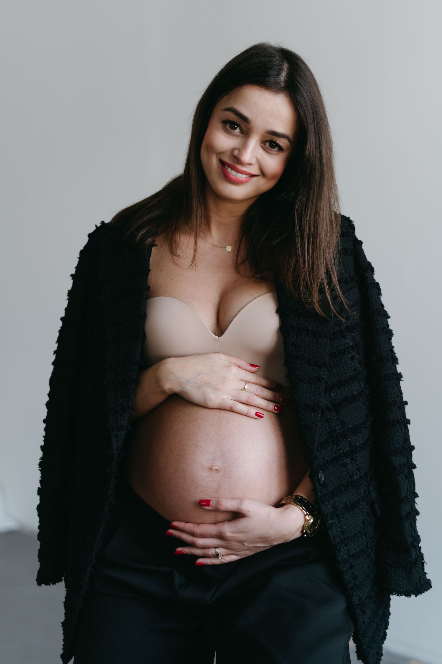 Stylish maternity portrait of an expectant mother wearing a black cardigan while caressing her baby bump.