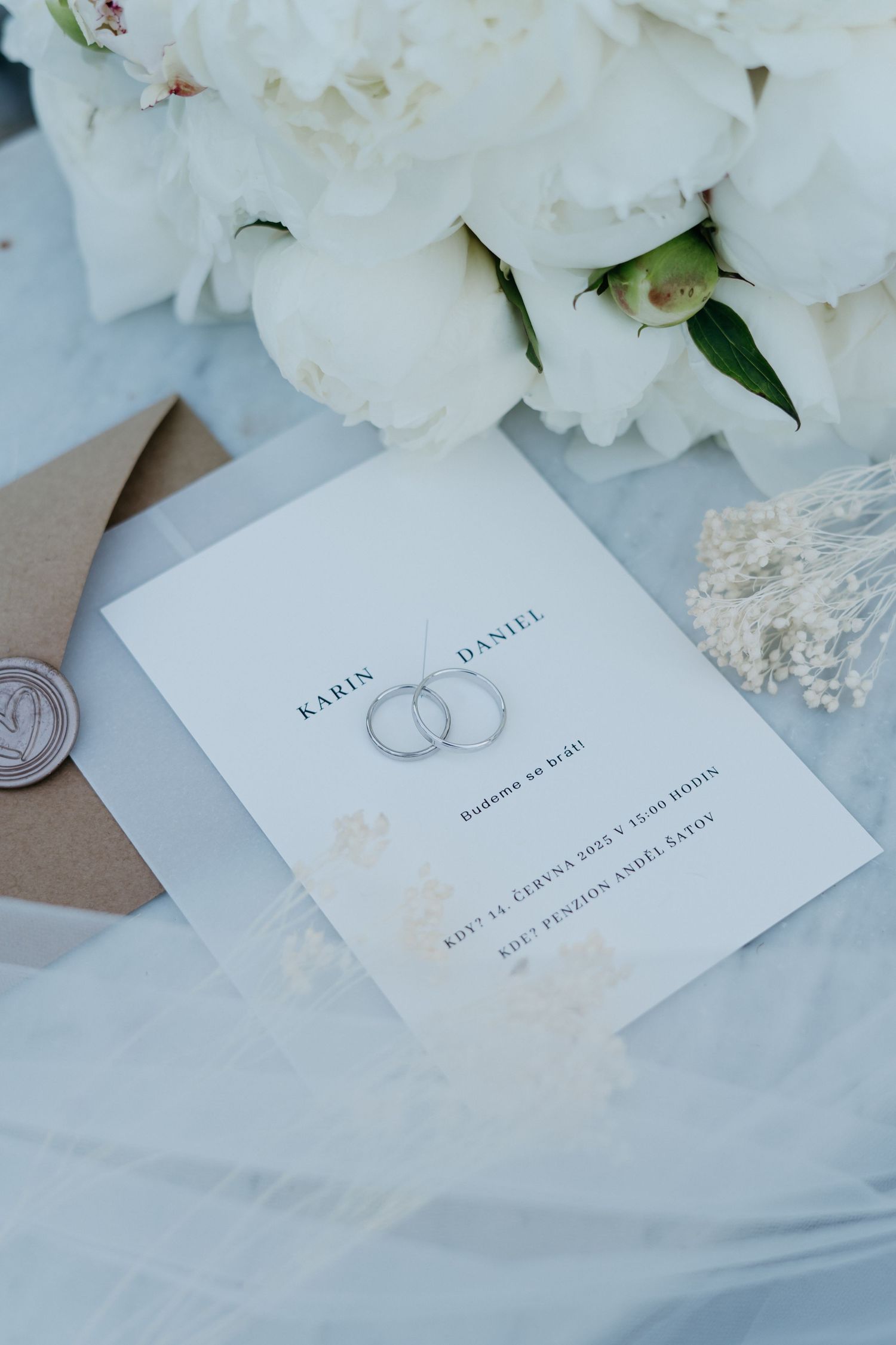 A wedding invitation with two linked rings design lies beside white flowers and a wax-sealed envelope.