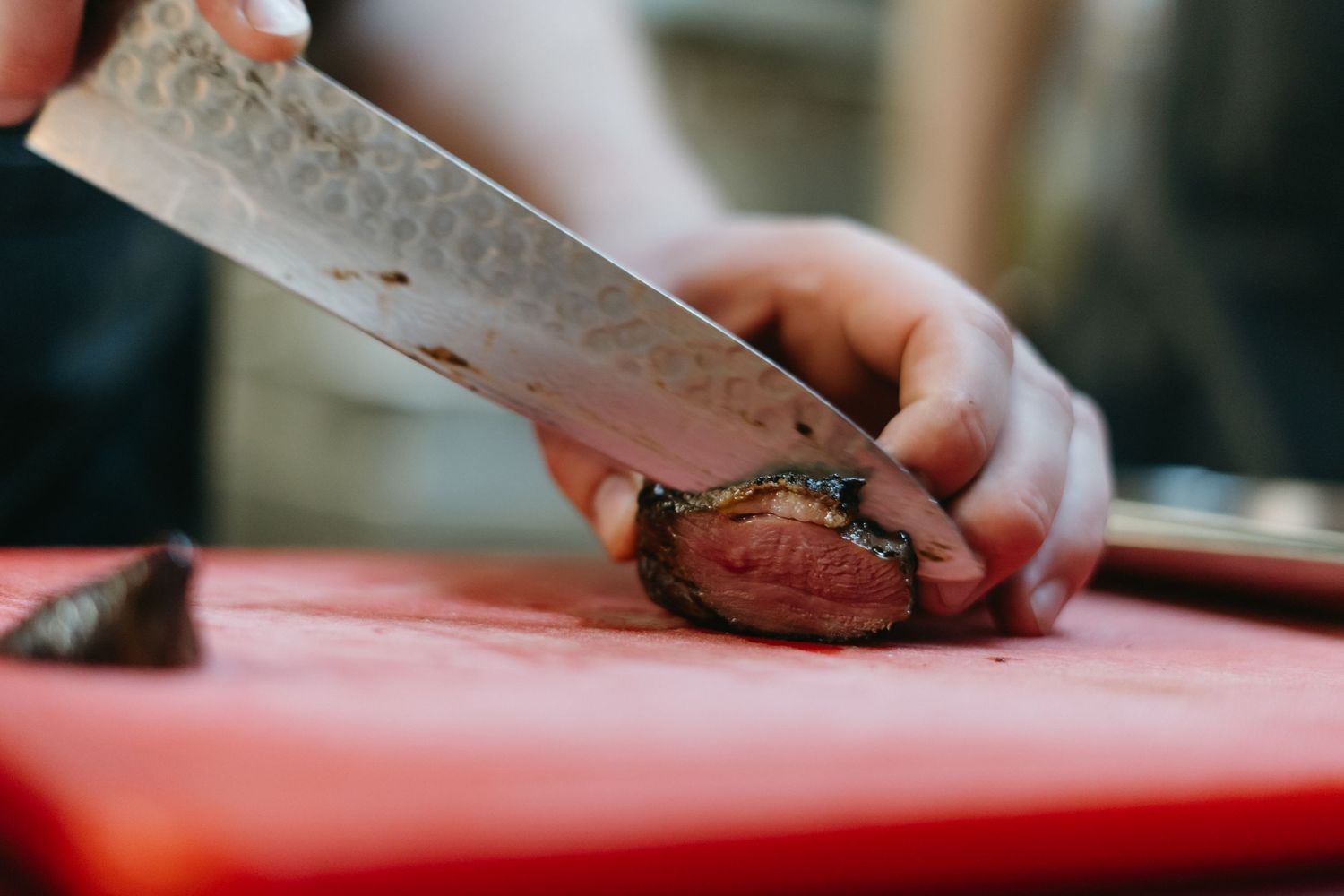 Chef's hands precisely slice sashimi with a sharp knife on a red cutting board in a professional kitchen setting.
