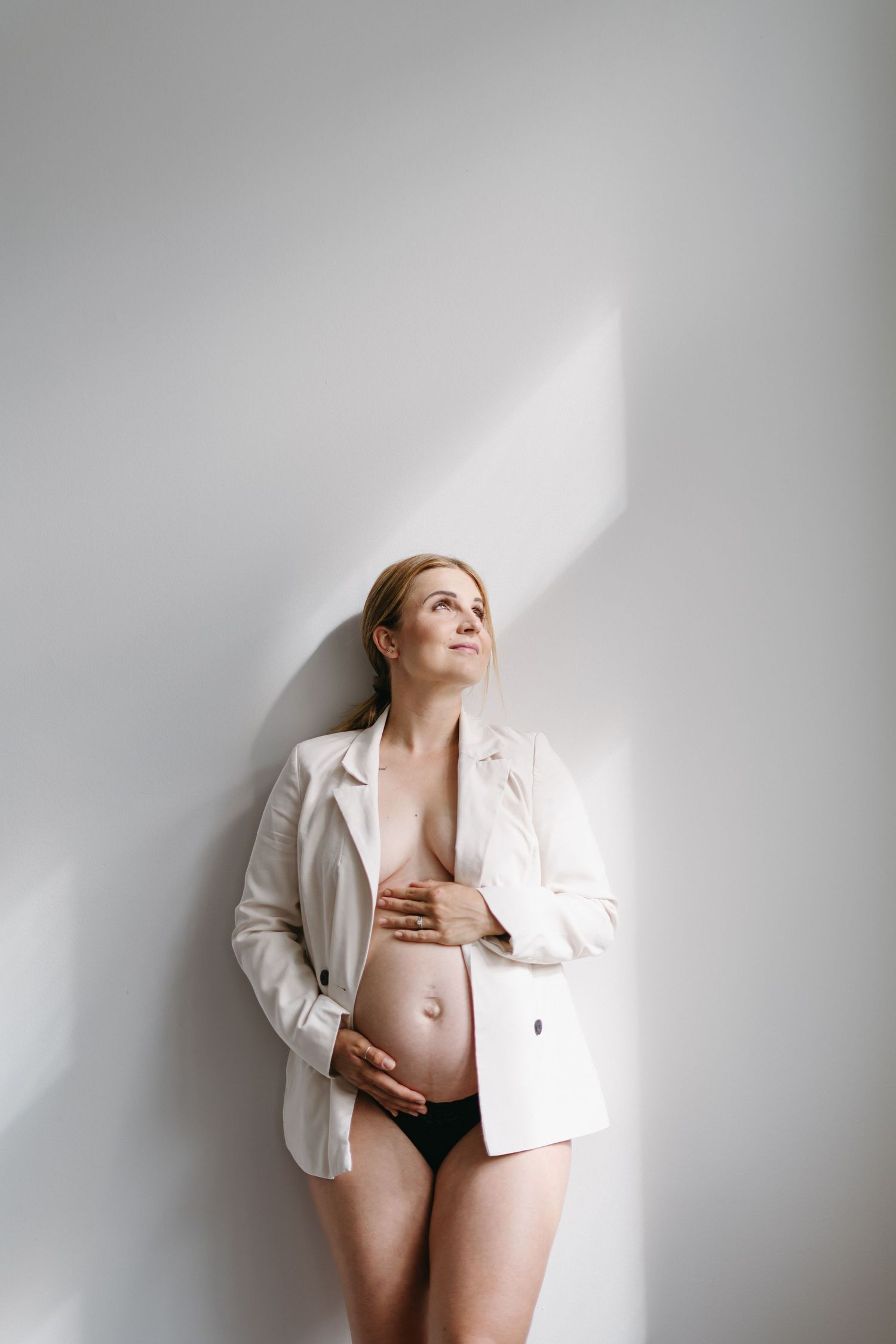 Artistic maternity photos against white wall showcase growing belly in minimalist style.