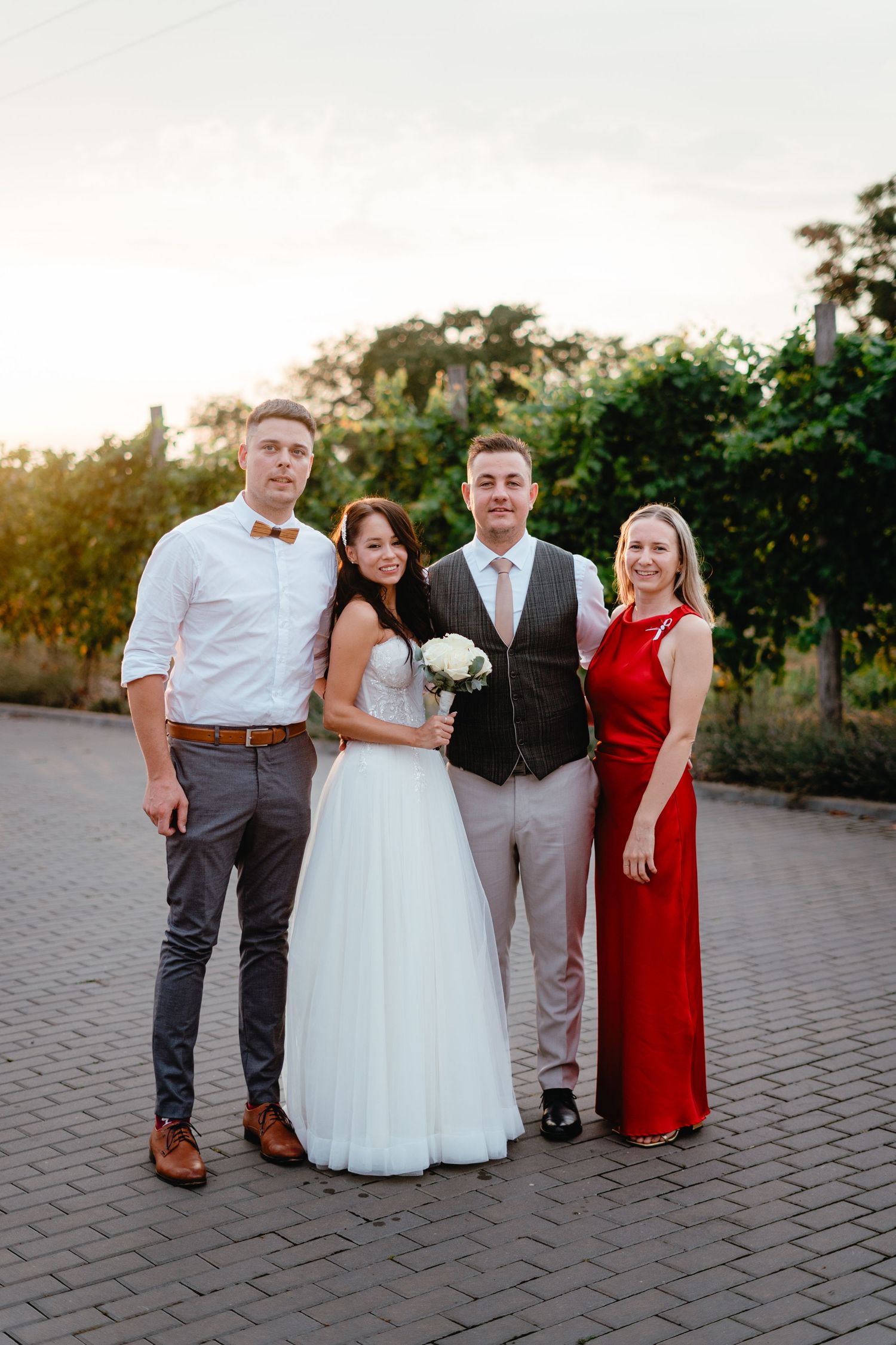 Wedding party of four posing at sunset on a brick path.