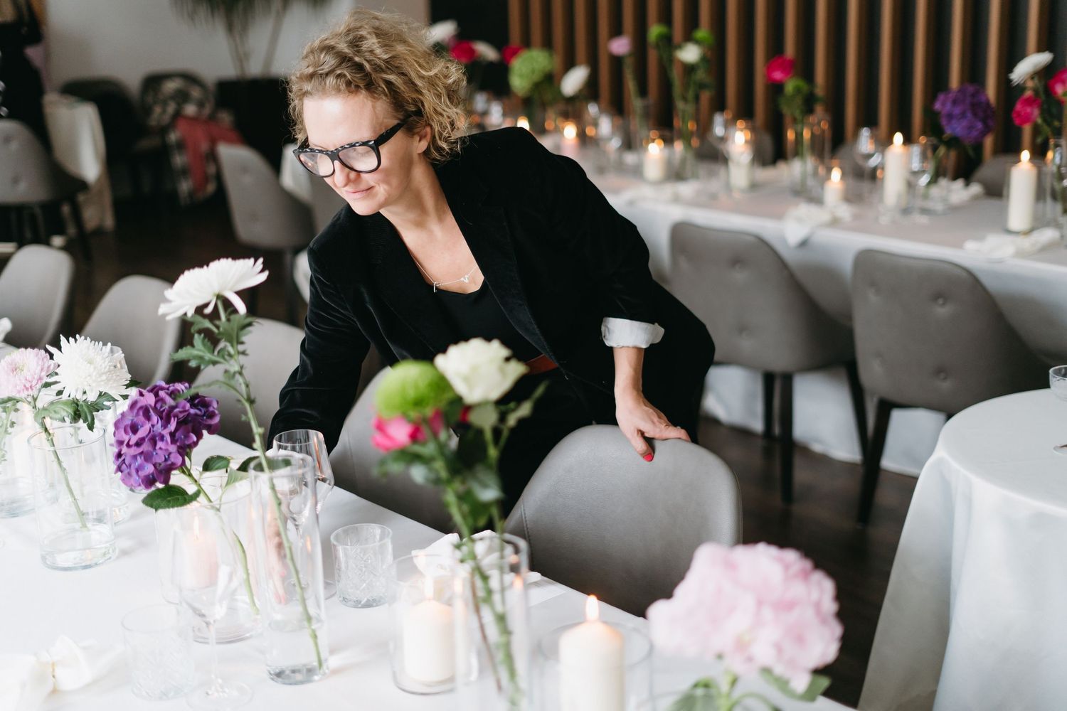 Event planner arranging floral centerpieces on elegant white tablescapes.