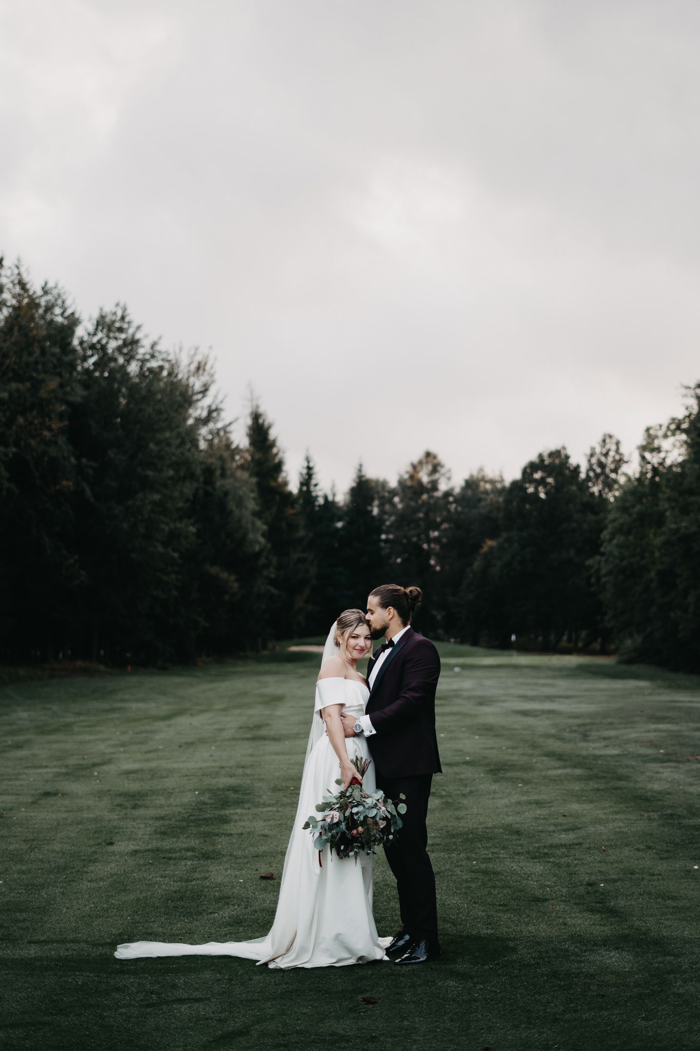 A couple shares an intimate moment on a misty golf course during their wedding day photo session.