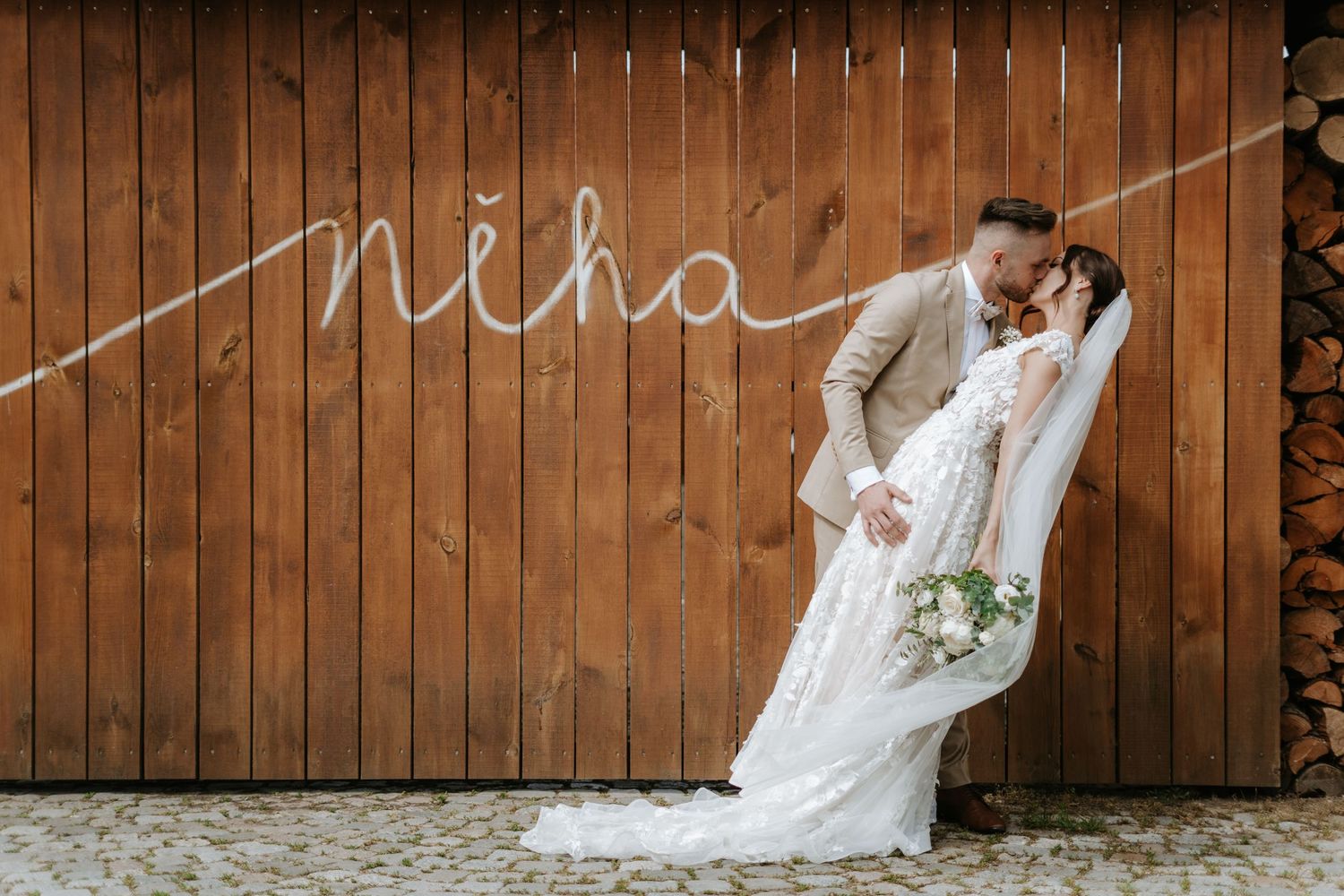 A romantic wedding couple poses in front of rustic wooden wall with cursive neon 'Nicha' sign.