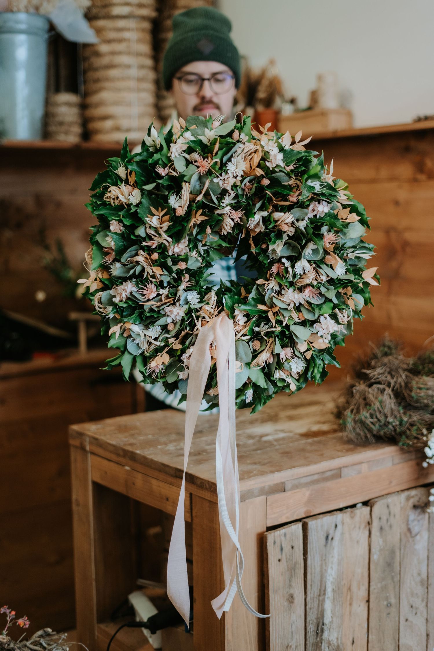 Beautiful handcrafted wreath made with fresh greenery and white ribbon displayed on wooden furniture.