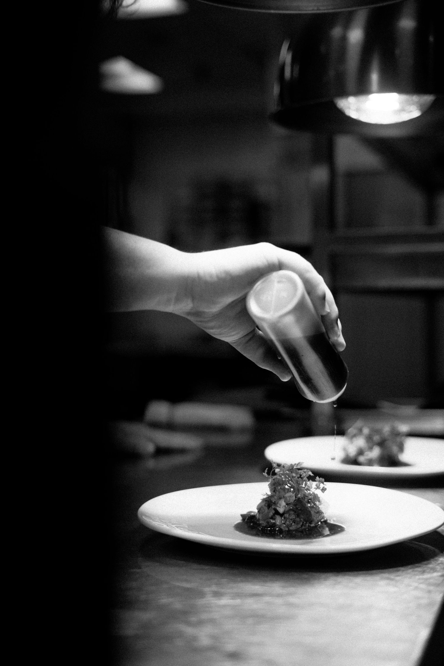 Black and white sequence of plates being prepared in a restaurant kitchen showing fine dining presentation.