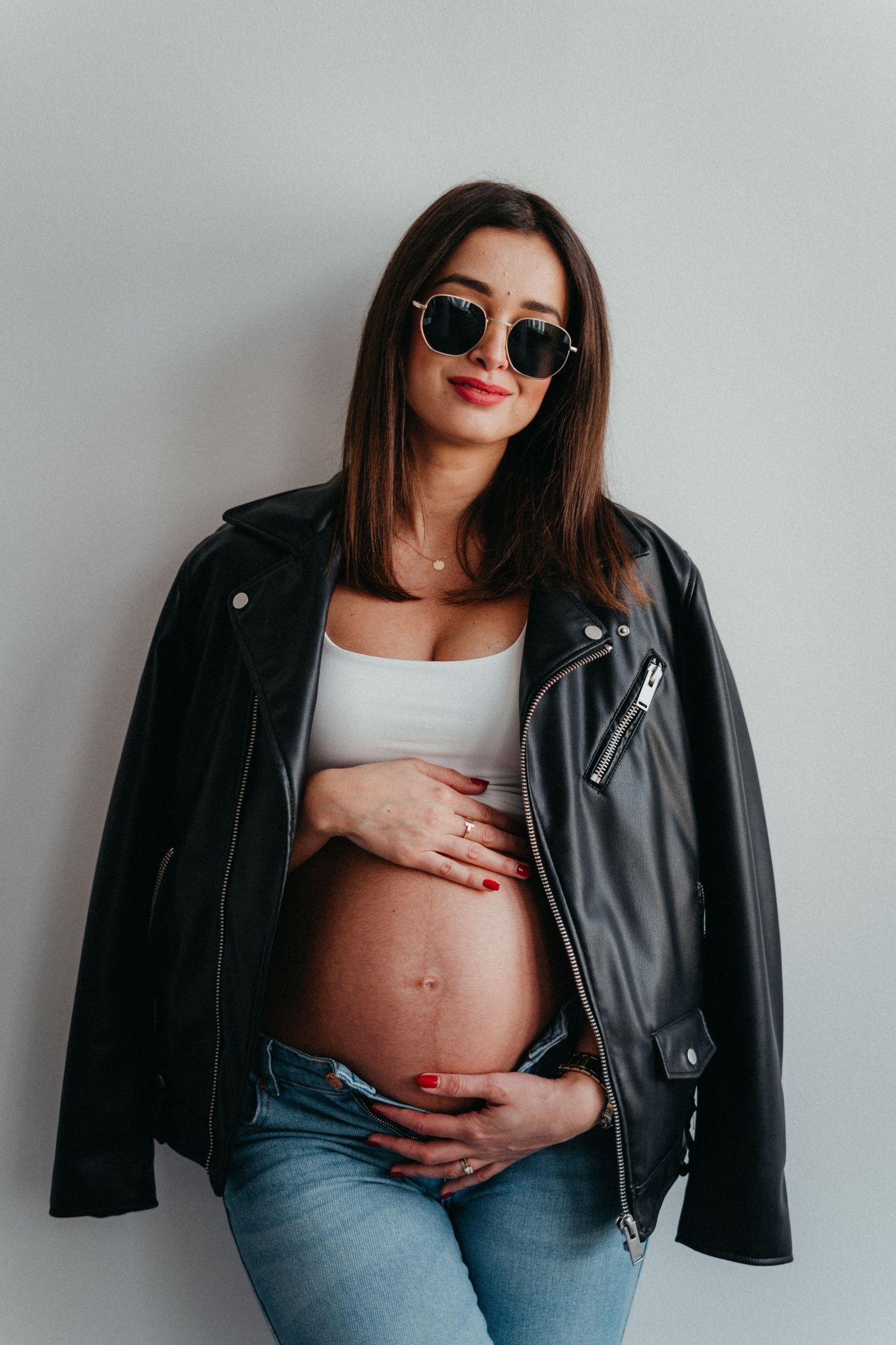 Minimalist studio maternity portrait with woman in leather jacket and jeans.
