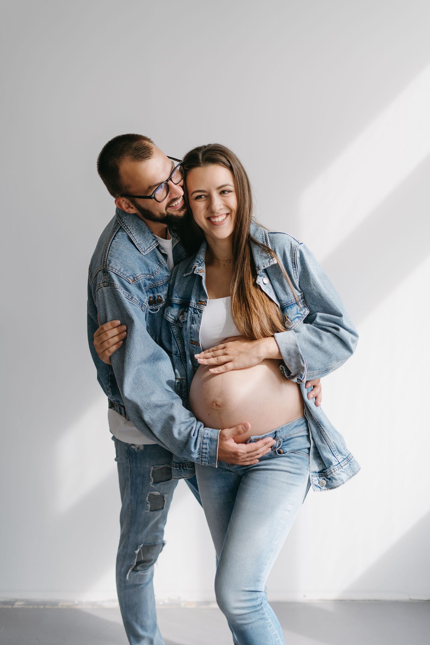 Couple in denim embracing in bright minimalist studio setting showing affection and joy.
