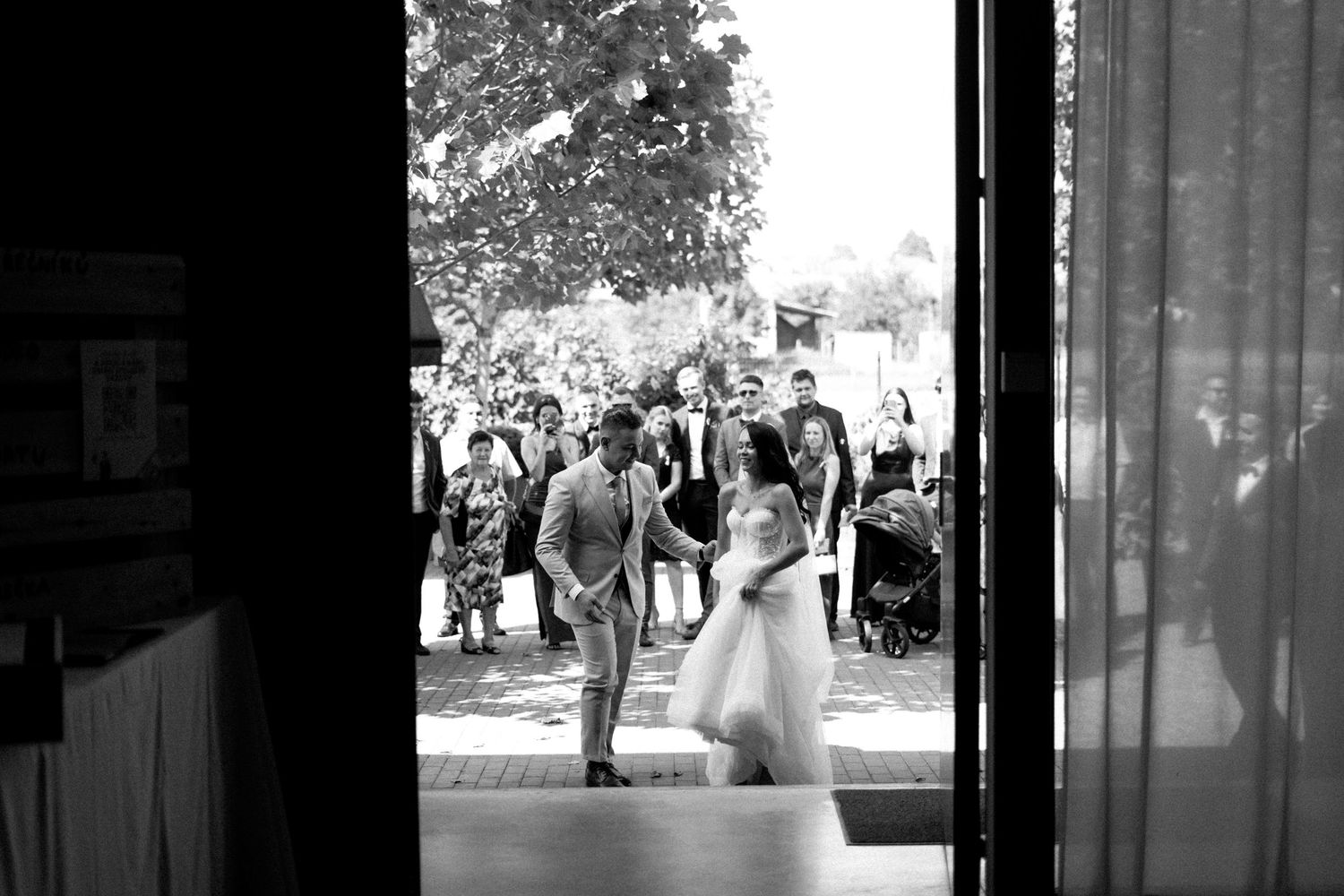 Black and white photo of a couple dancing in a doorway surrounded by guests.
