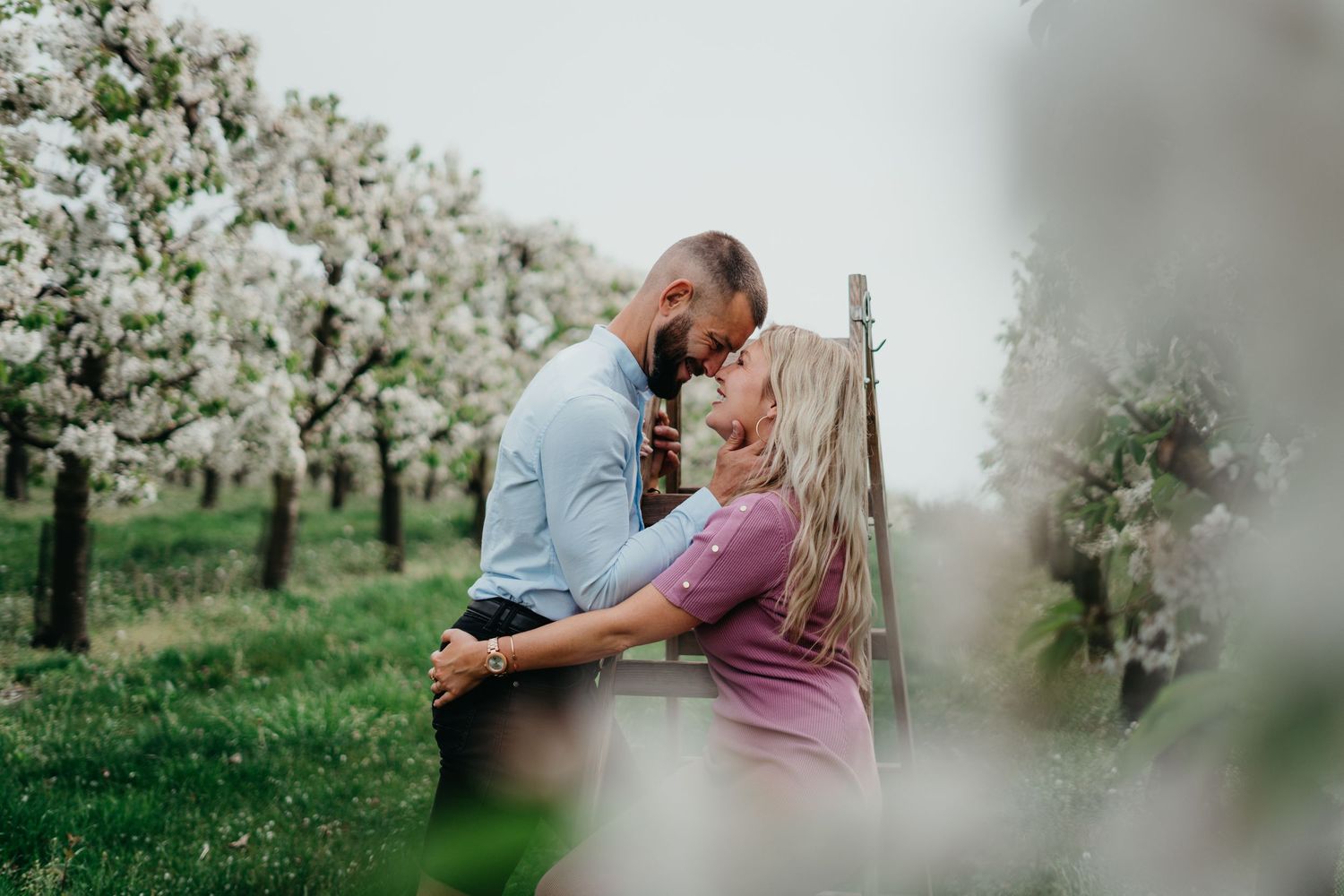 Romantic couple embracing in blooming spring orchard during maternity photoshoot.