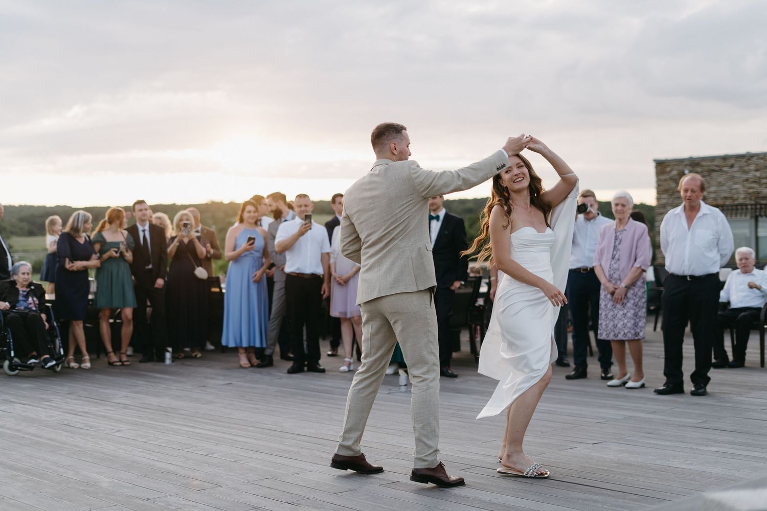 A couple dances together at their rooftop wedding reception during sunset as guests watch from the sidelines.