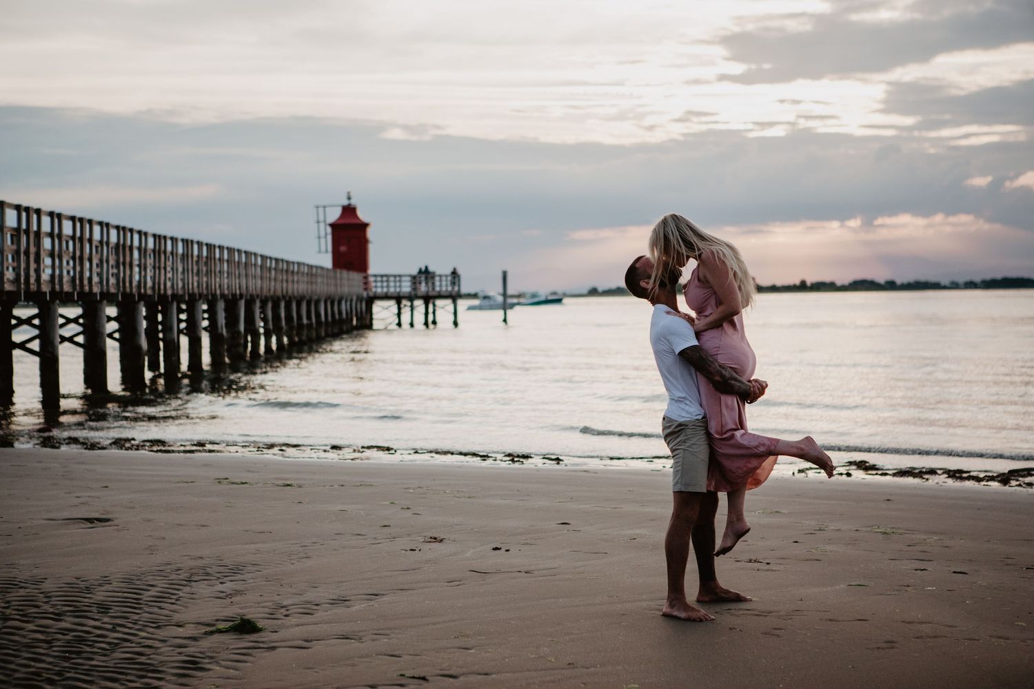 Couple embracing near lighthouse pier during sunset.