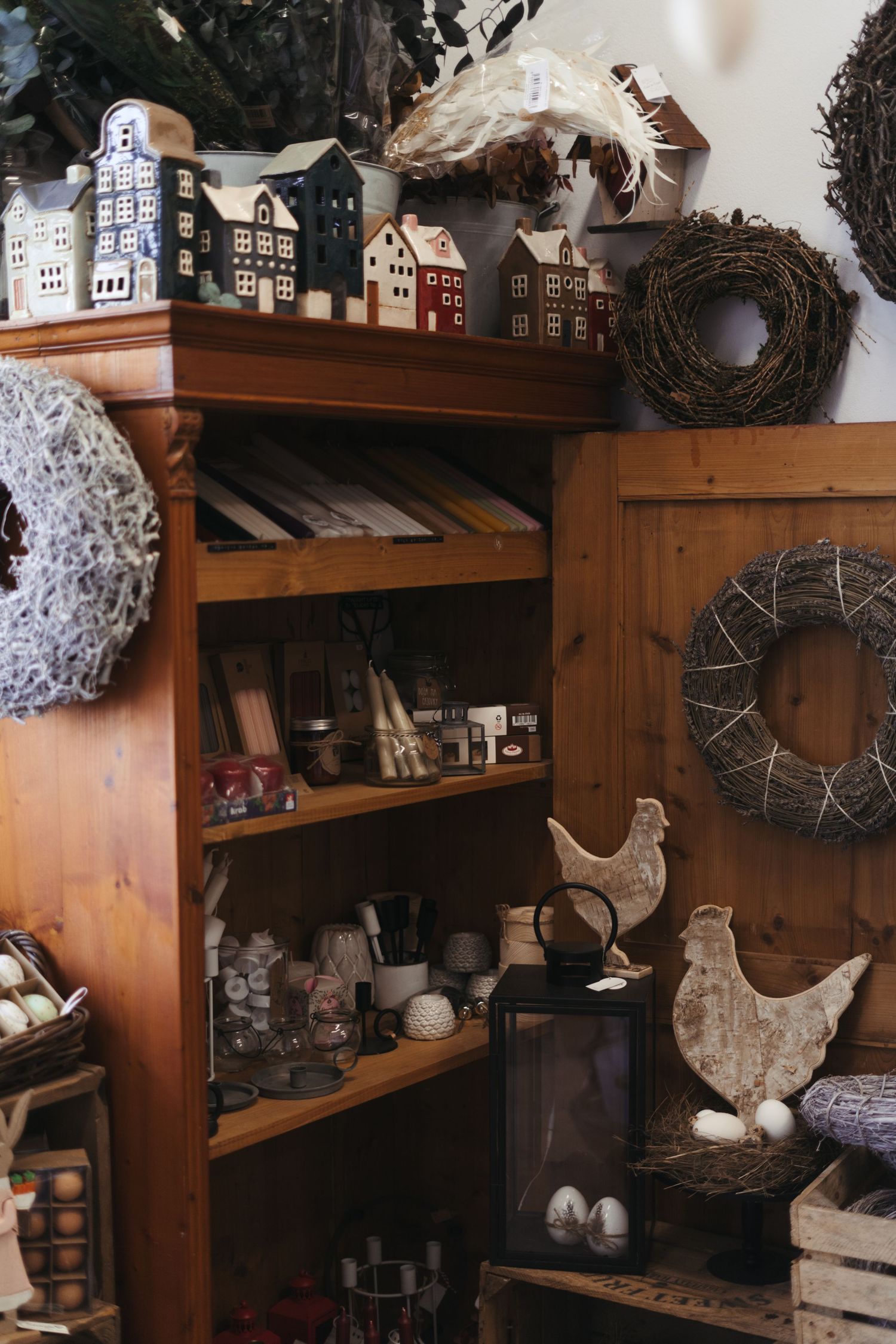Rustic wooden shelves display decorative model houses, wreaths, and ceramic chickens in a cozy cottage-style arrangement.