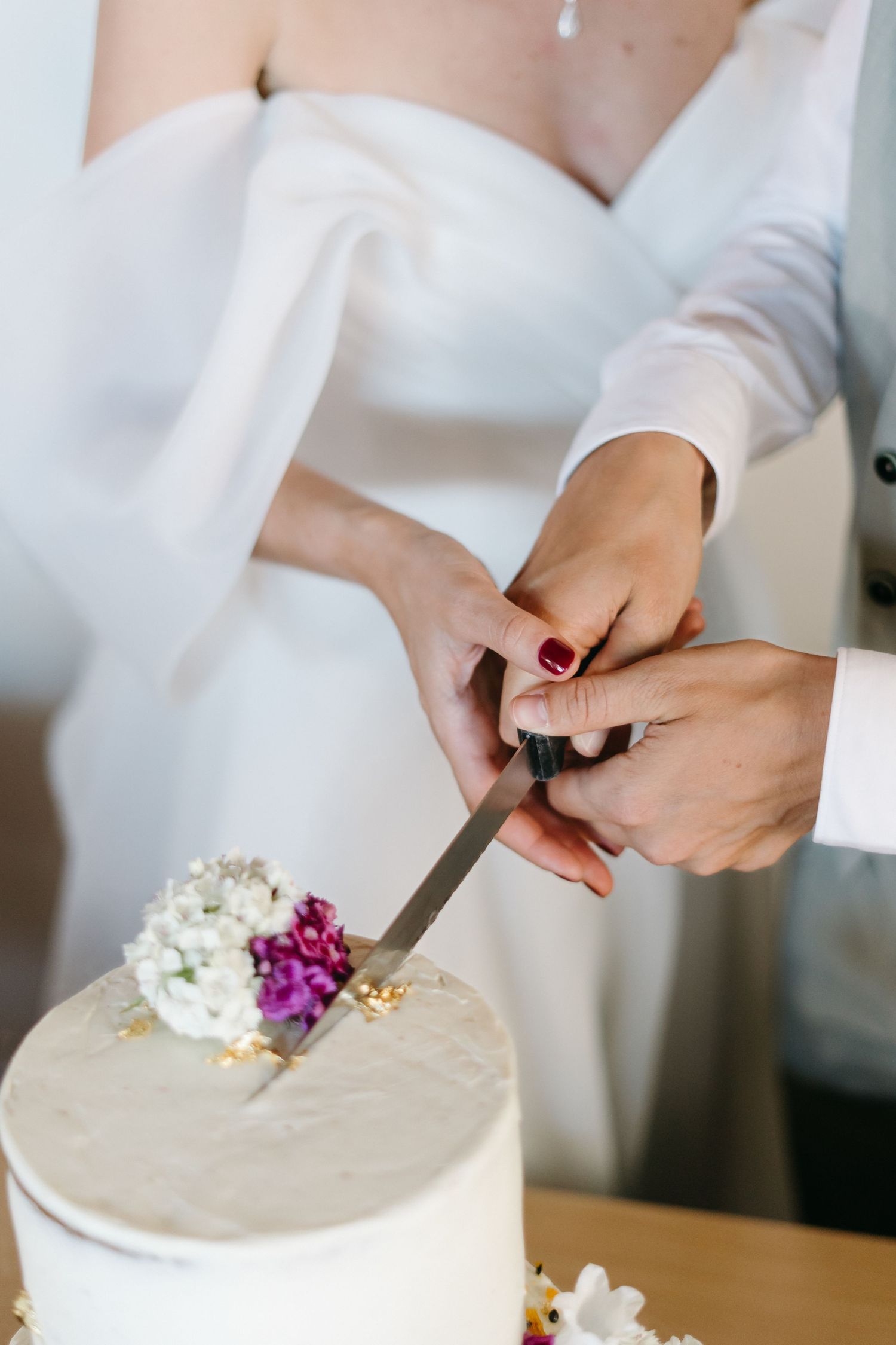 Close-up view of hands decorating a white frosted cake with fresh purple flowers.