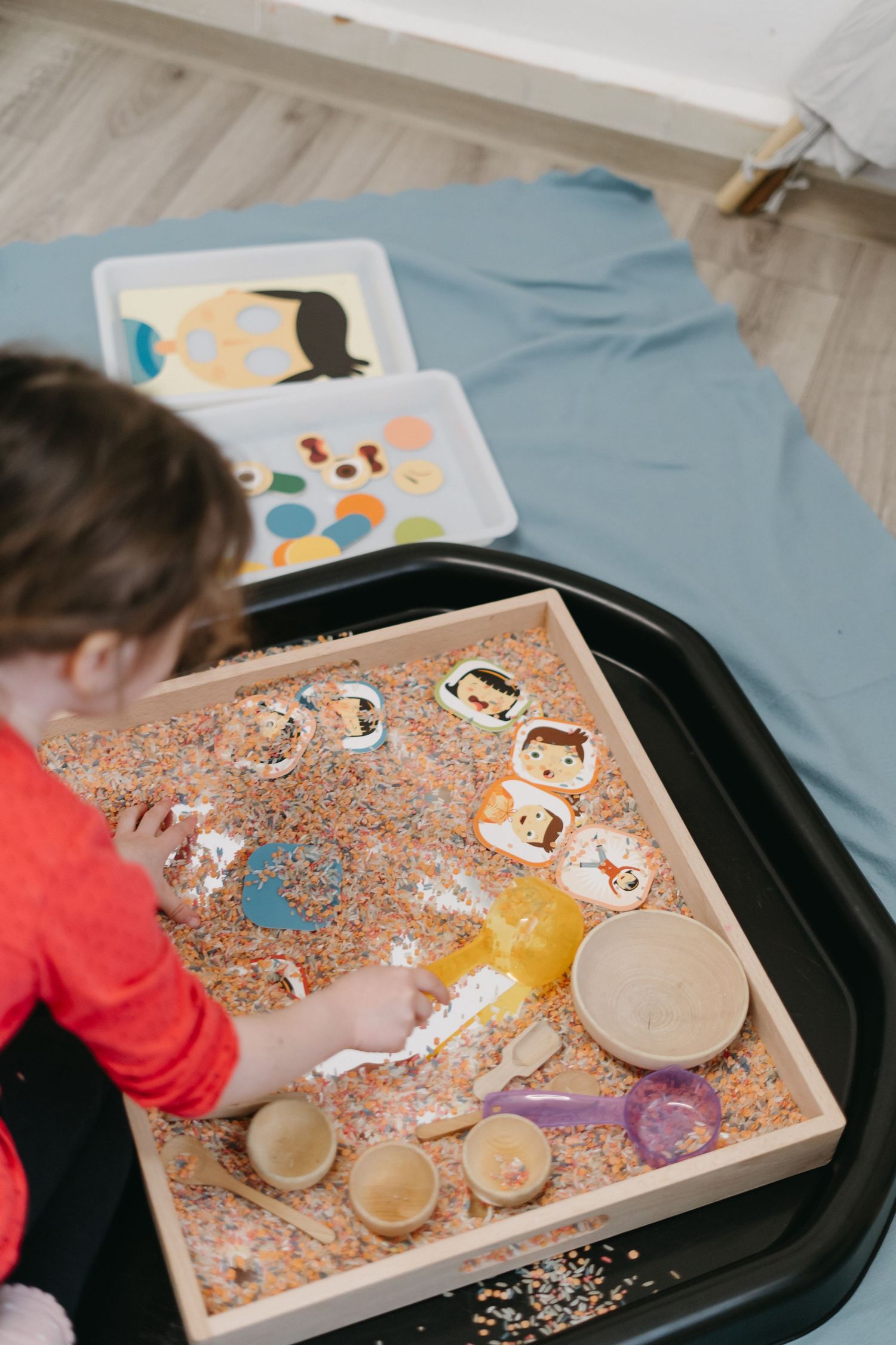Sensory play activity showing wooden toys in a tray filled with kinetic sand and loose materials for exploration and learning.