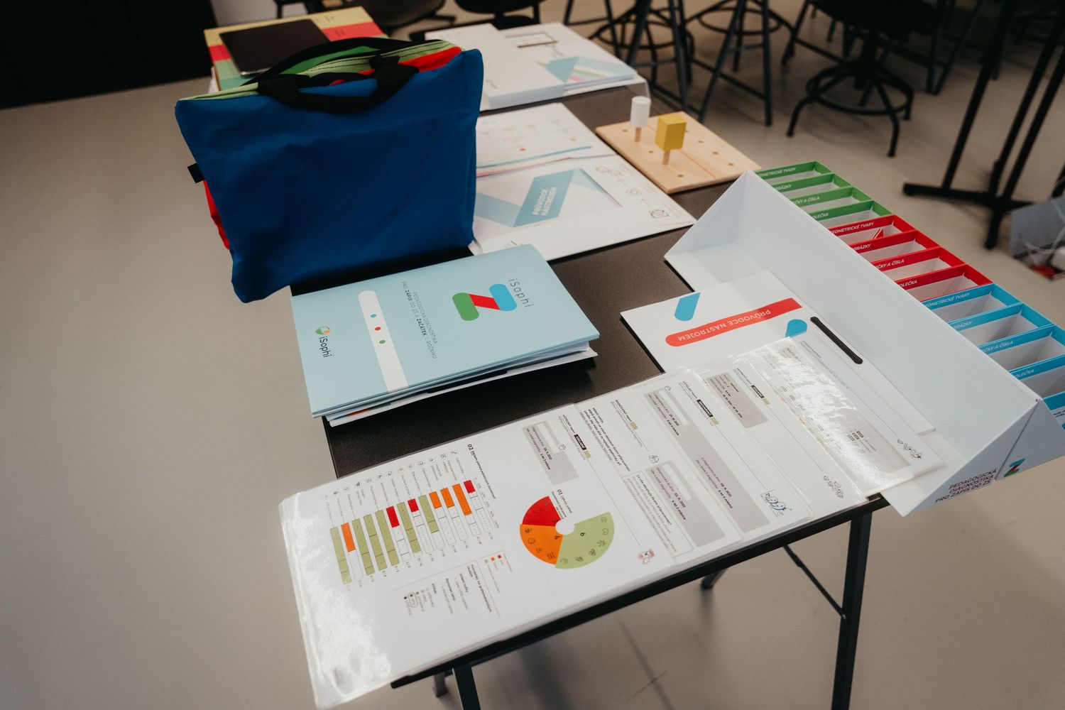 Classroom desk with scattered educational materials including notebooks, papers with colorful charts, and a blue bag.