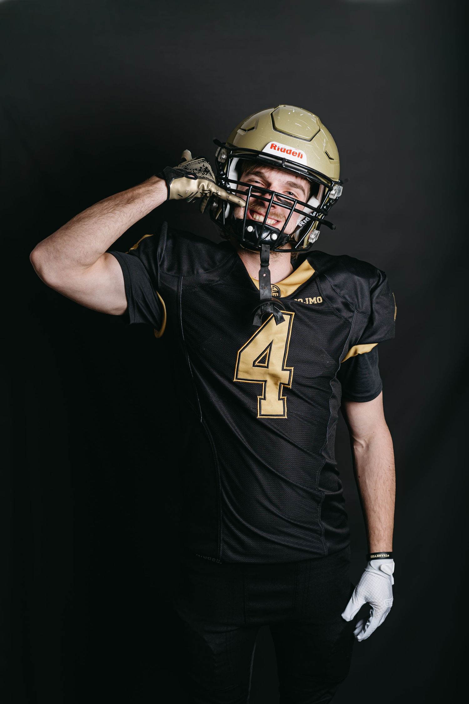 Professional footballer in black uniform wearing helmet and gloves performing a catching motion sequence against dark background.