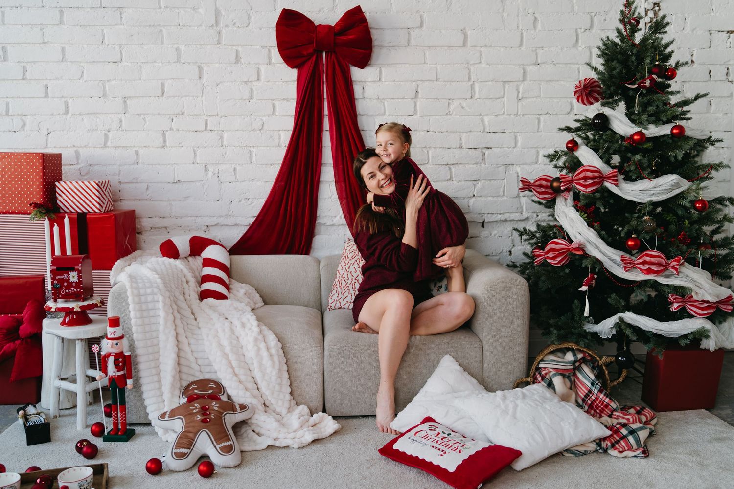 Mother and daughter share a festive hug on a sofa surrounded by Christmas gifts and a decorated tree.