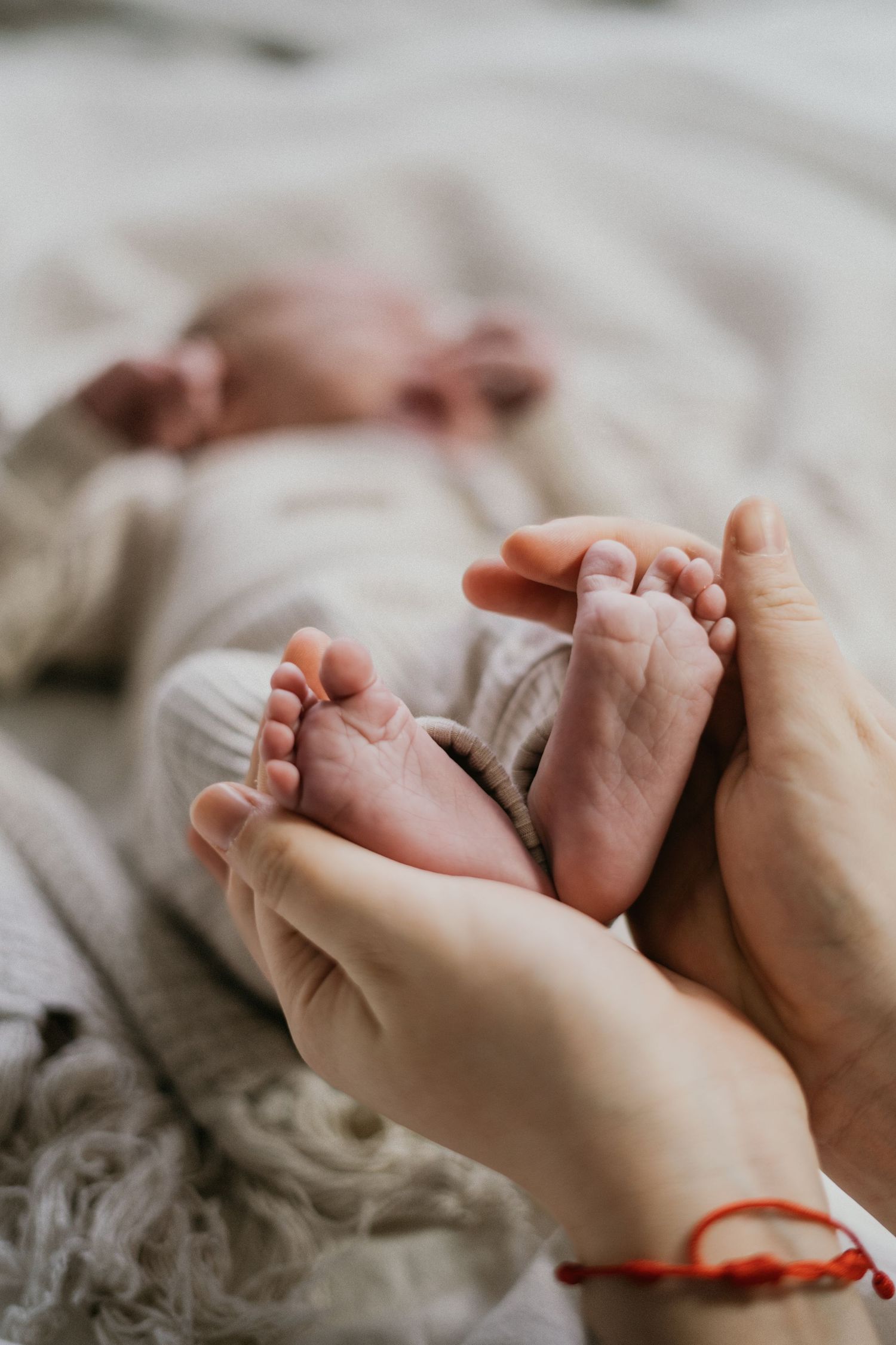 Gentle hands holding tiny newborn baby feet against soft white blanket in intimate close-up shot.