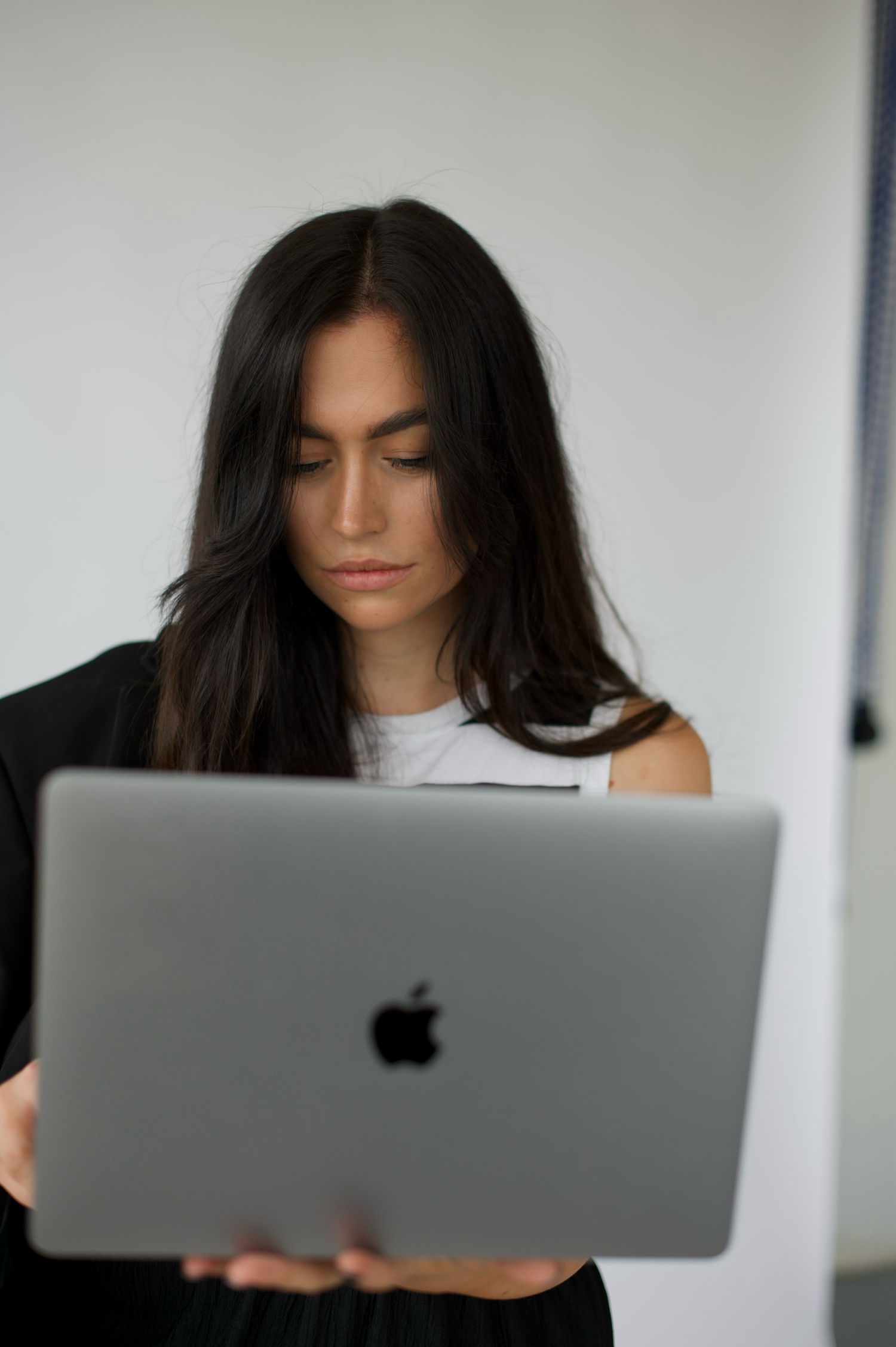Woman working on MacBook laptop in minimal white office setting.