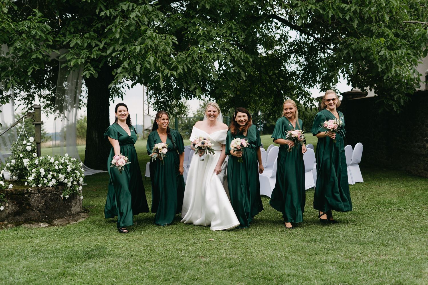 Wedding party stands in a line outdoors in coordinated green and white attire on a grassy lawn.