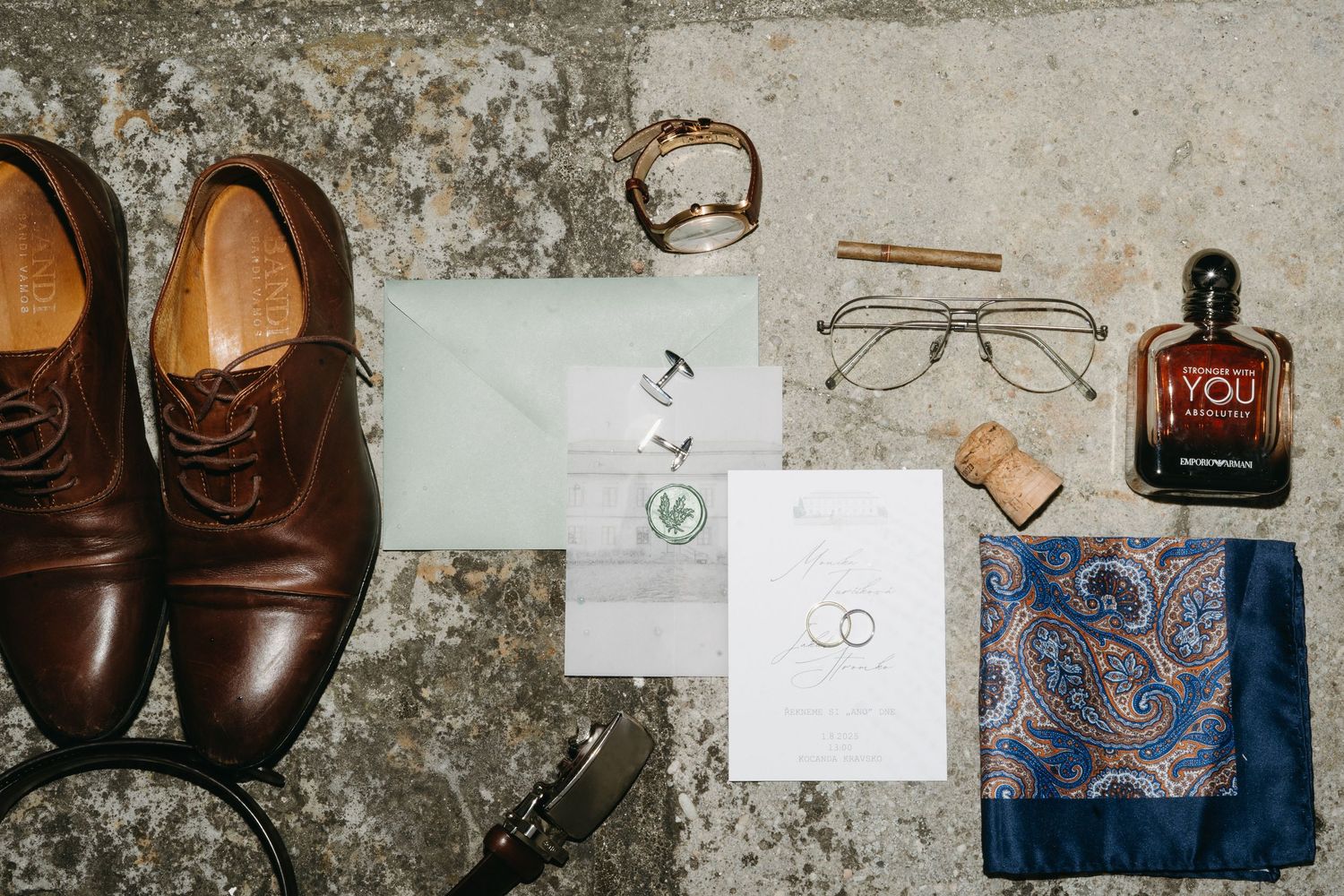Groom wedding flat lay with brown leather oxford shoes, paisley pocket square, glasses, cologne, cufflinks, and invitation suite.