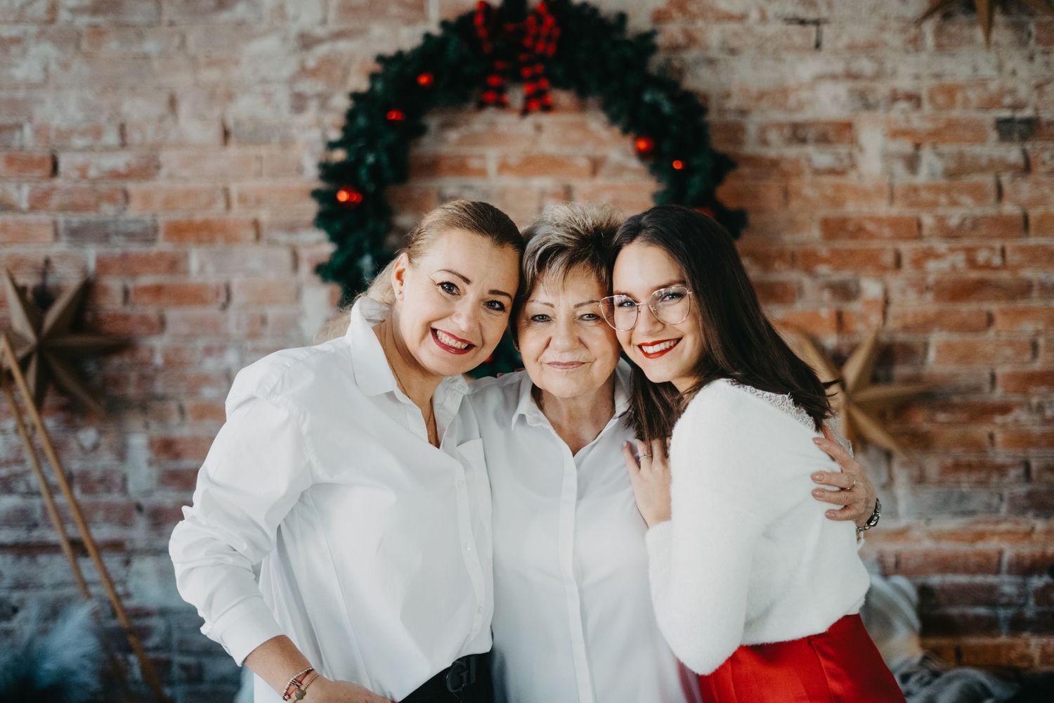 Family wearing white poses against rustic brick wall during portrait photo session.