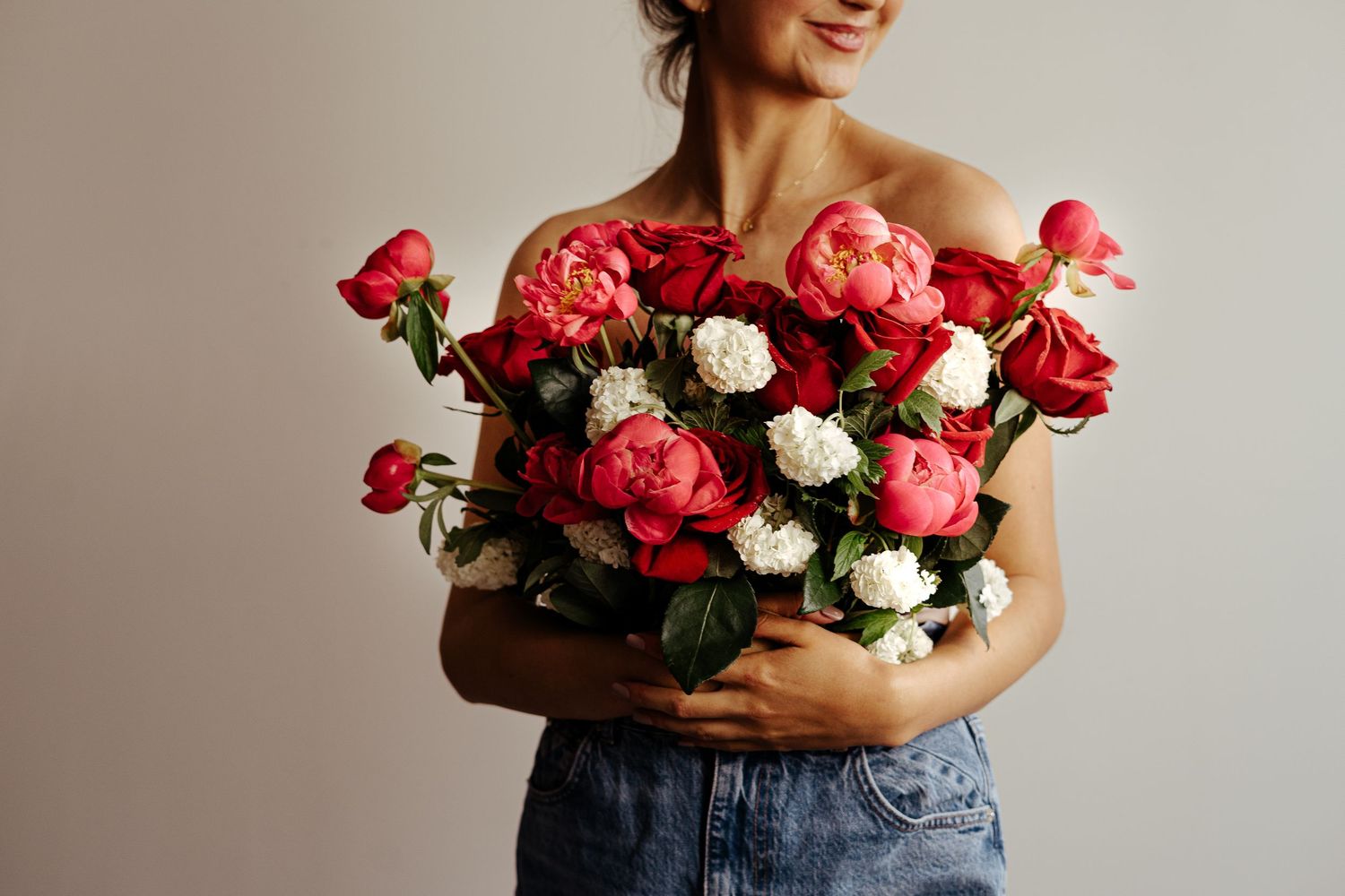 Person holding a stunning bouquet of pink and red roses against a light background.