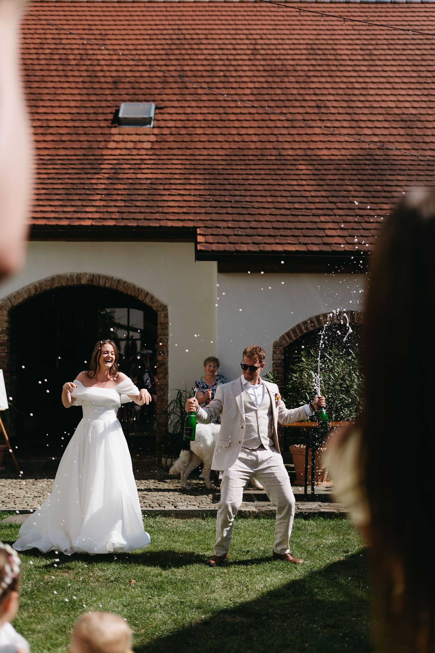 Celebration at an outdoor summer wedding with playful moments captured in front of a traditional building with red rooftop.