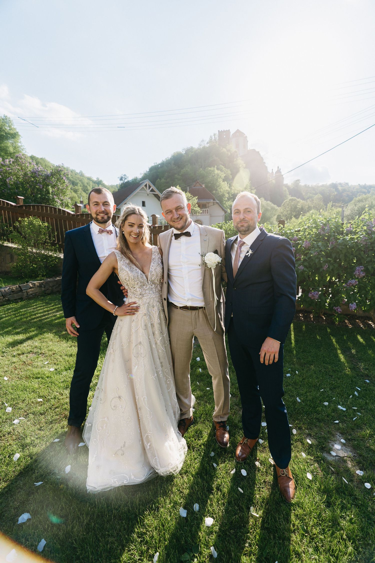 Wedding party poses together on a sunny lawn with mountains in background and sun flares in the frame.