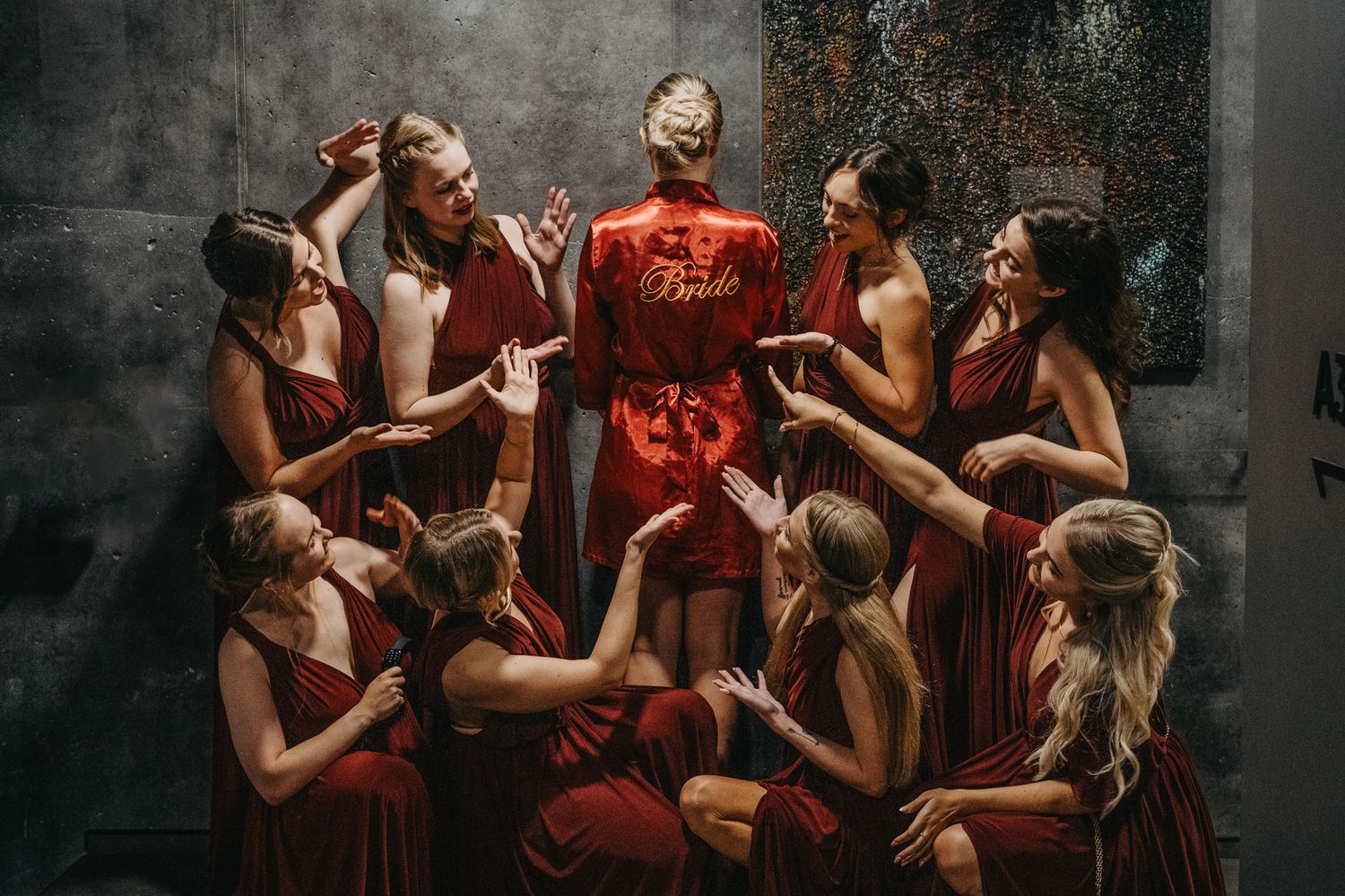 Group of dancers in matching red outfits pose together in dramatic lighting against industrial backdrop.