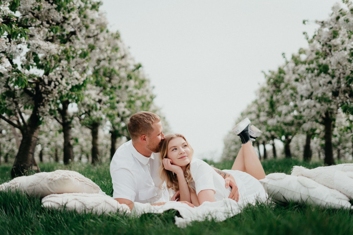 Couple lying on white blankets in a blooming orchard during spring.