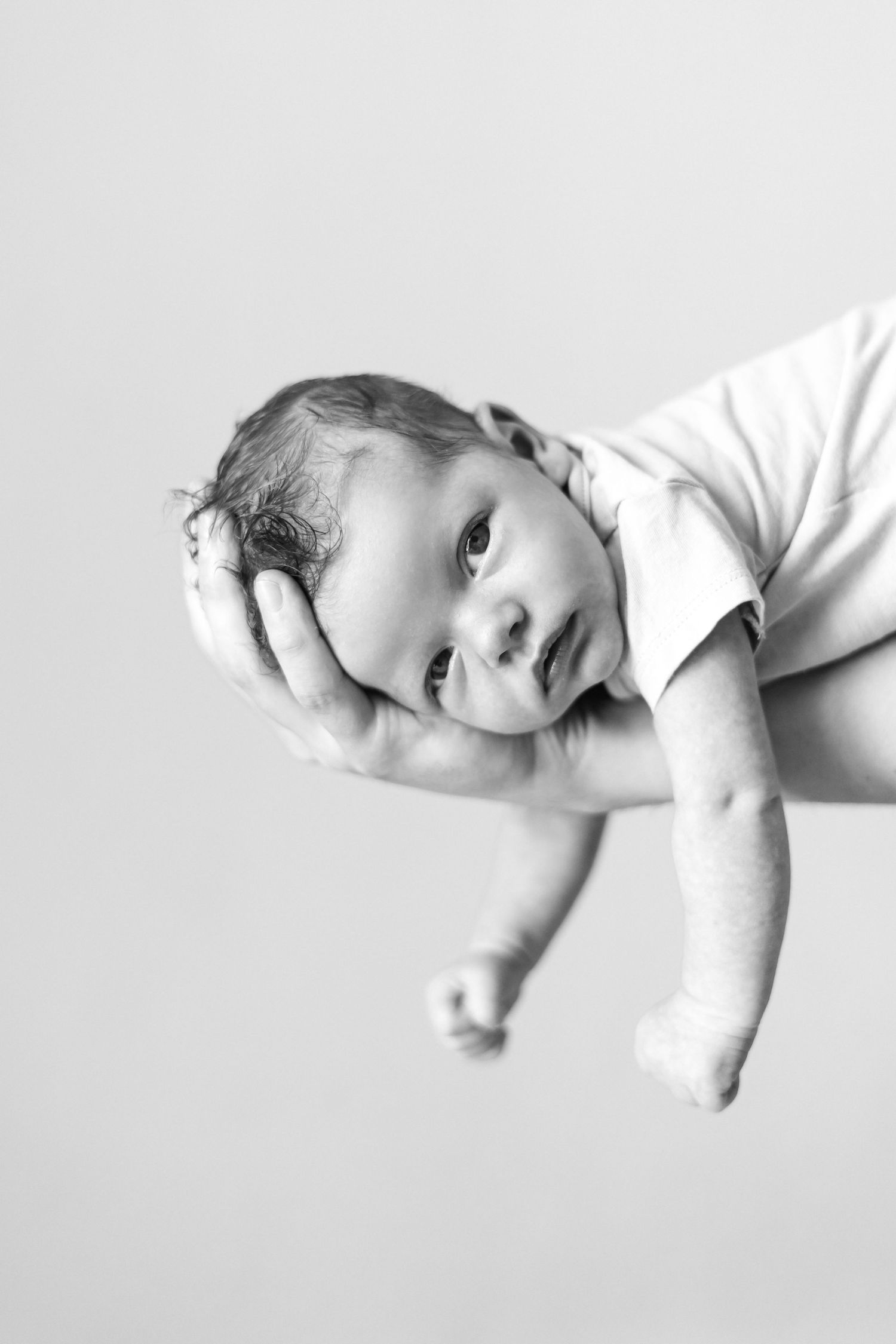 Black and white portrait of an infant being held up against a plain background.