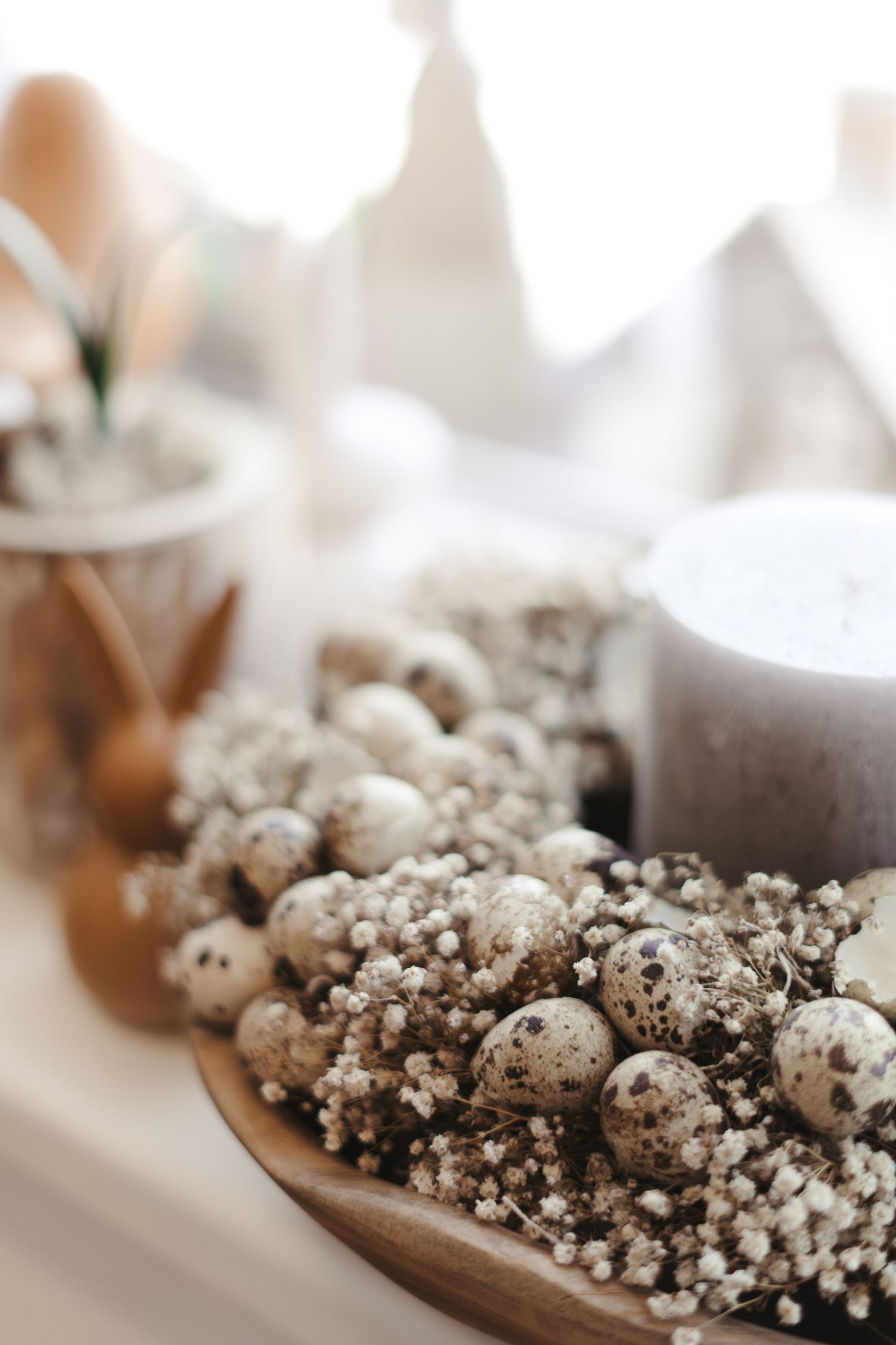 Small quail eggs and decorative sprigs arranged on a rustic wooden plate with soft bokeh background.