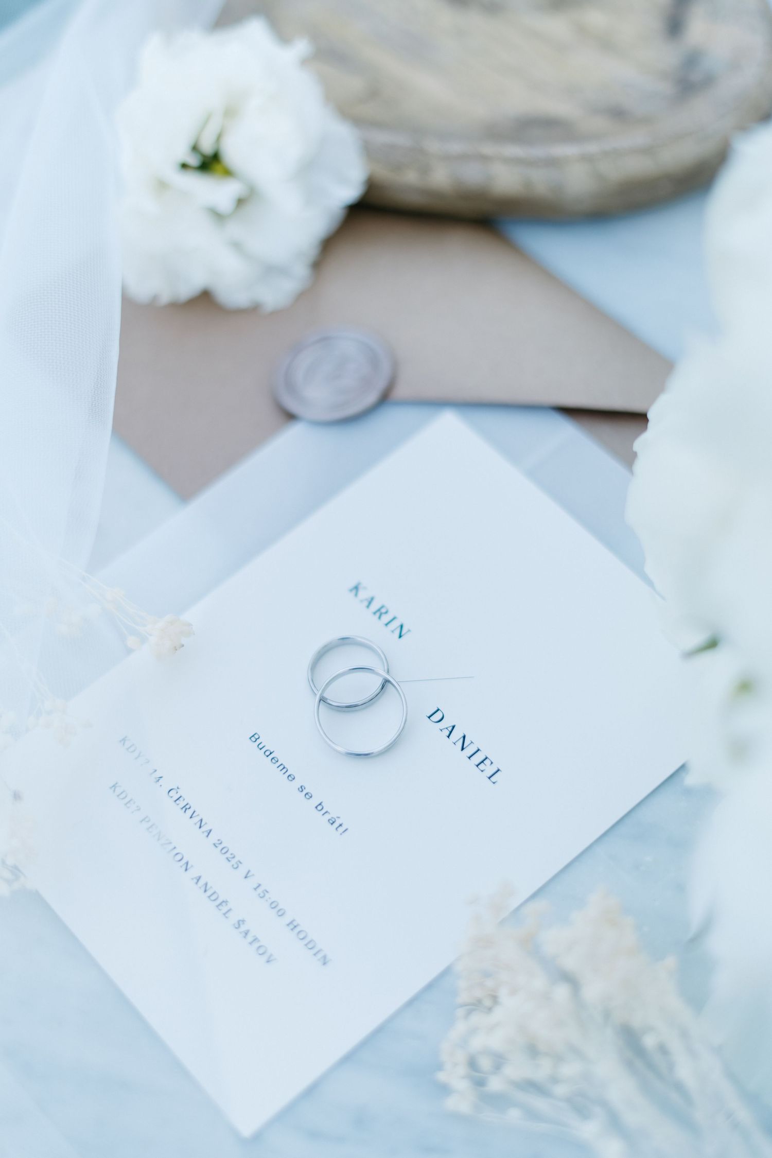 Simple white place cards and a wedding ring arranged elegantly with a delicate flower against a light background.